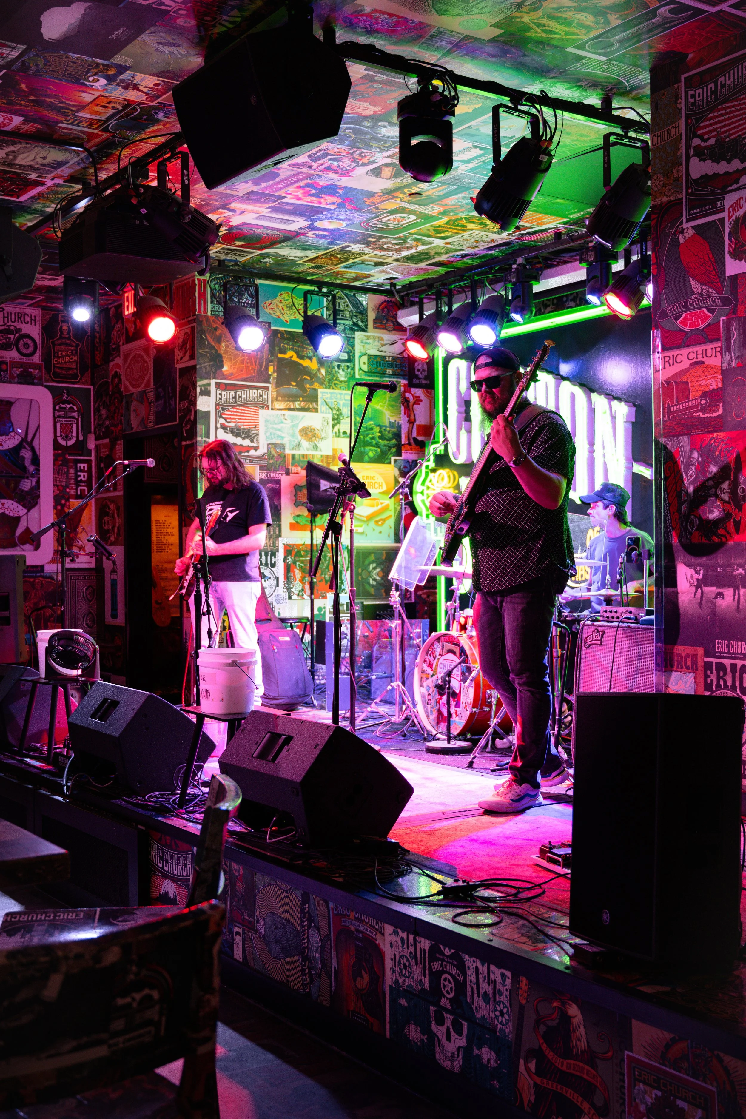 A band performing live on a colorful stage with punk rock posters and neon signs in the background, under vibrant stage lighting.