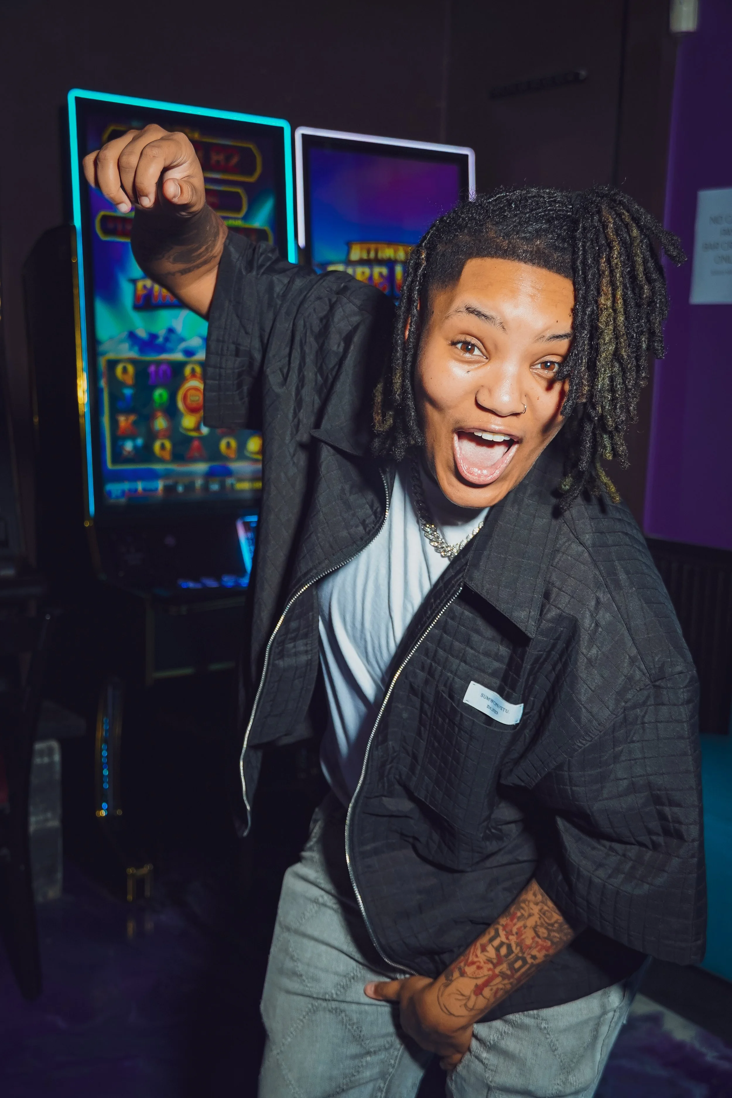 A person with dreadlocks and tattoos celebrating in front of a slot machine at a casino.