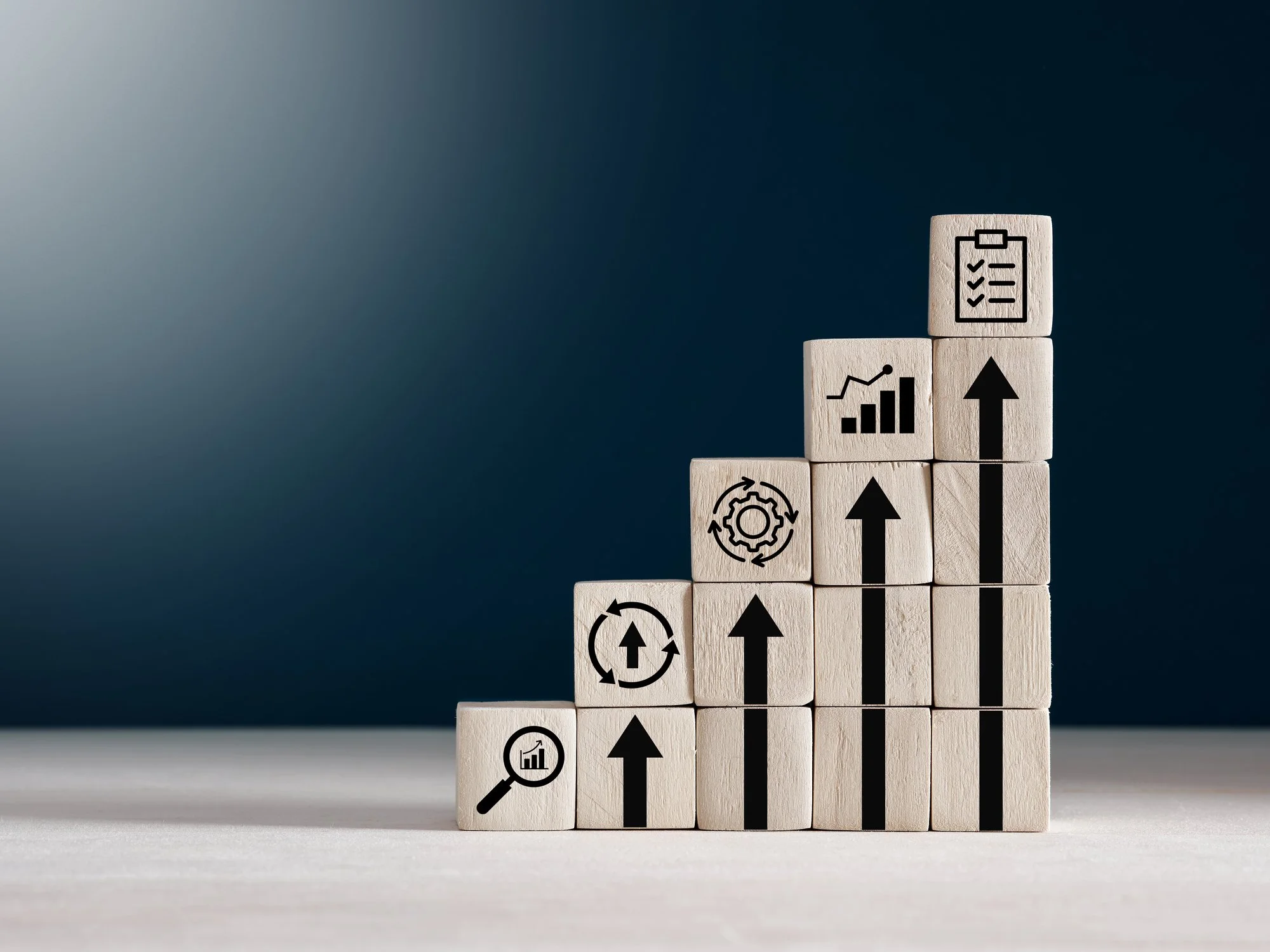 Wooden blocks arranged in ascending order with icons of graphs and arrows symbolizing growth and progress.