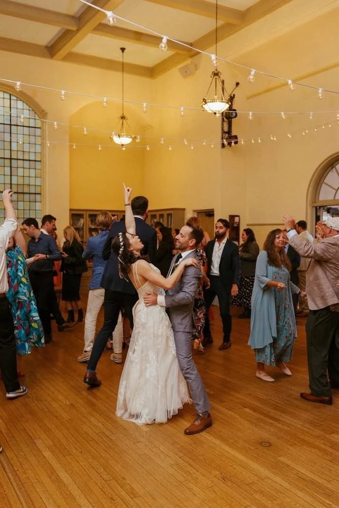 Bride and groom dancing at a wedding reception with guests dancing around them in a decorated hall with DJ Aeron