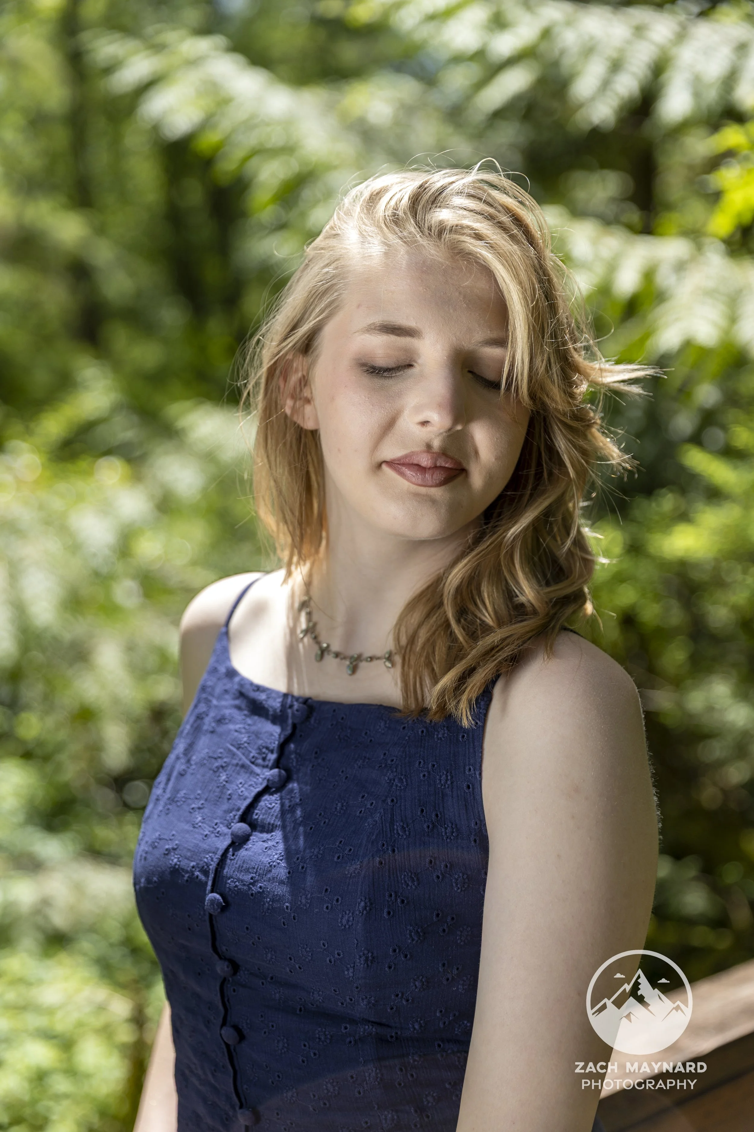 Teen girl in a navy dress in soft natural light among forest greenery during a summer senior portrait session in Snohomish County