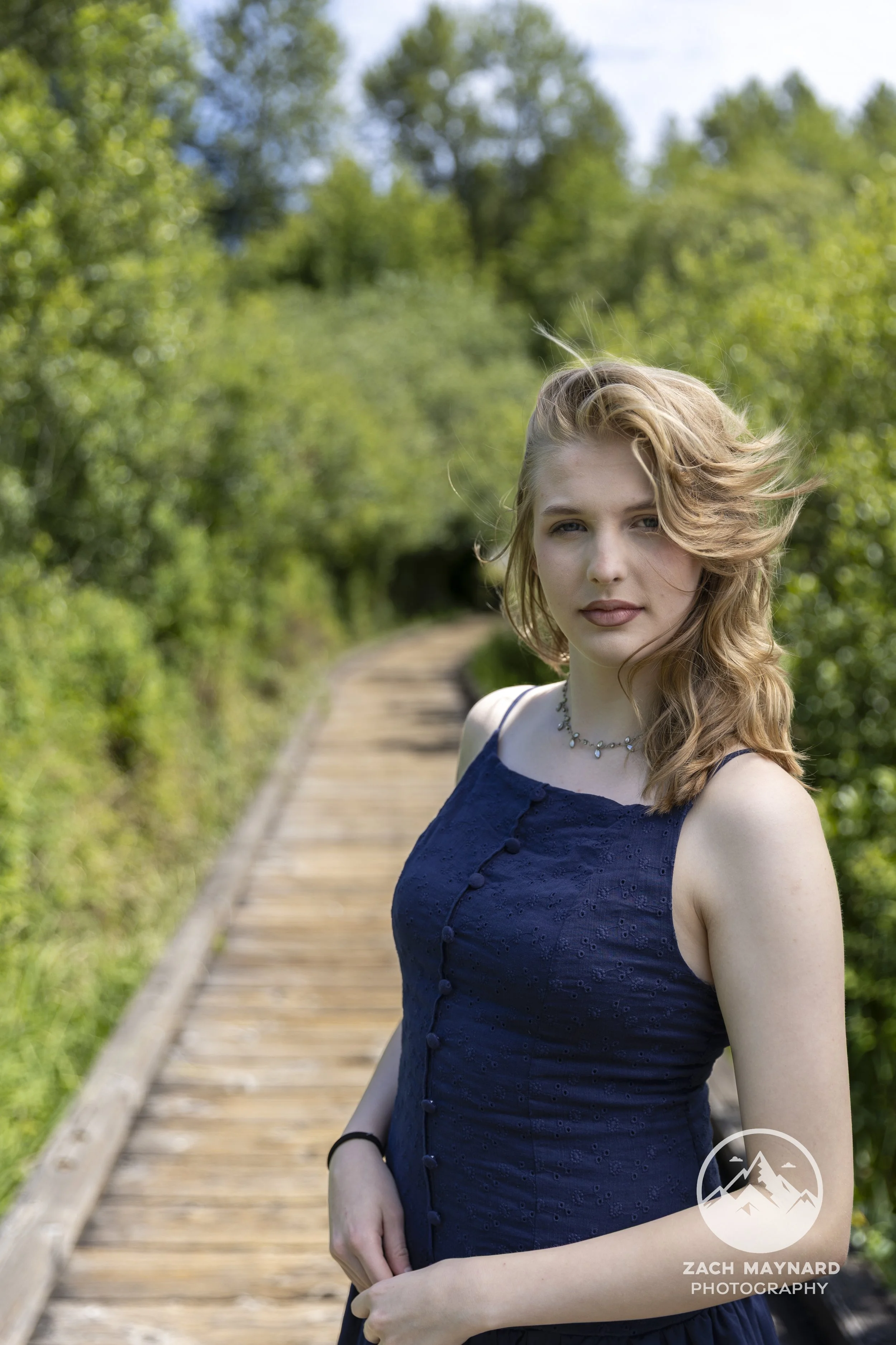 Teen girl in a navy dress on a wooden boardwalk trail during a summer senior portrait session in Snohomish County