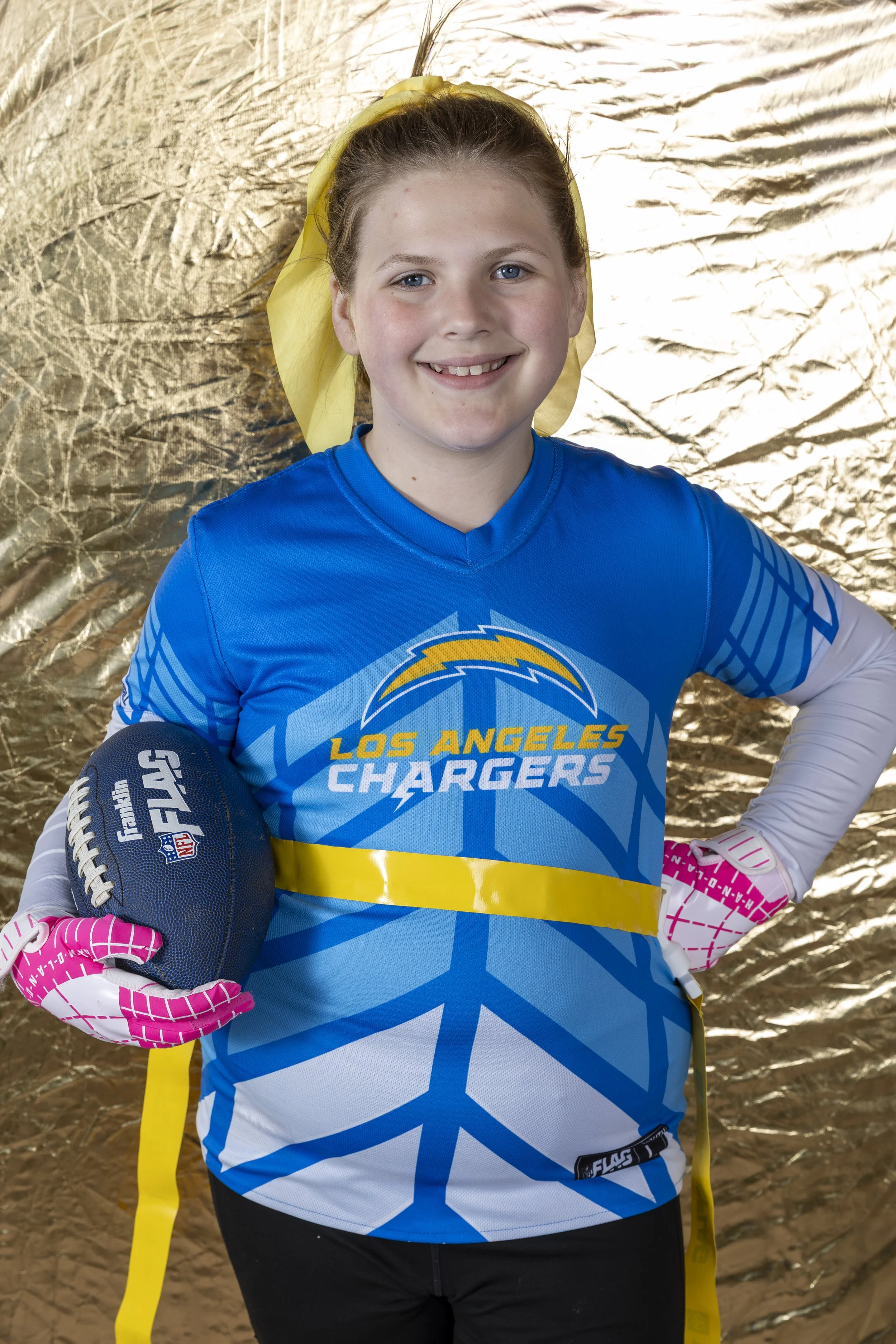 Youth flag football player in a Los Angeles Chargers uniform holding a football during a professional sports portrait session, showcasing youth sports photography.