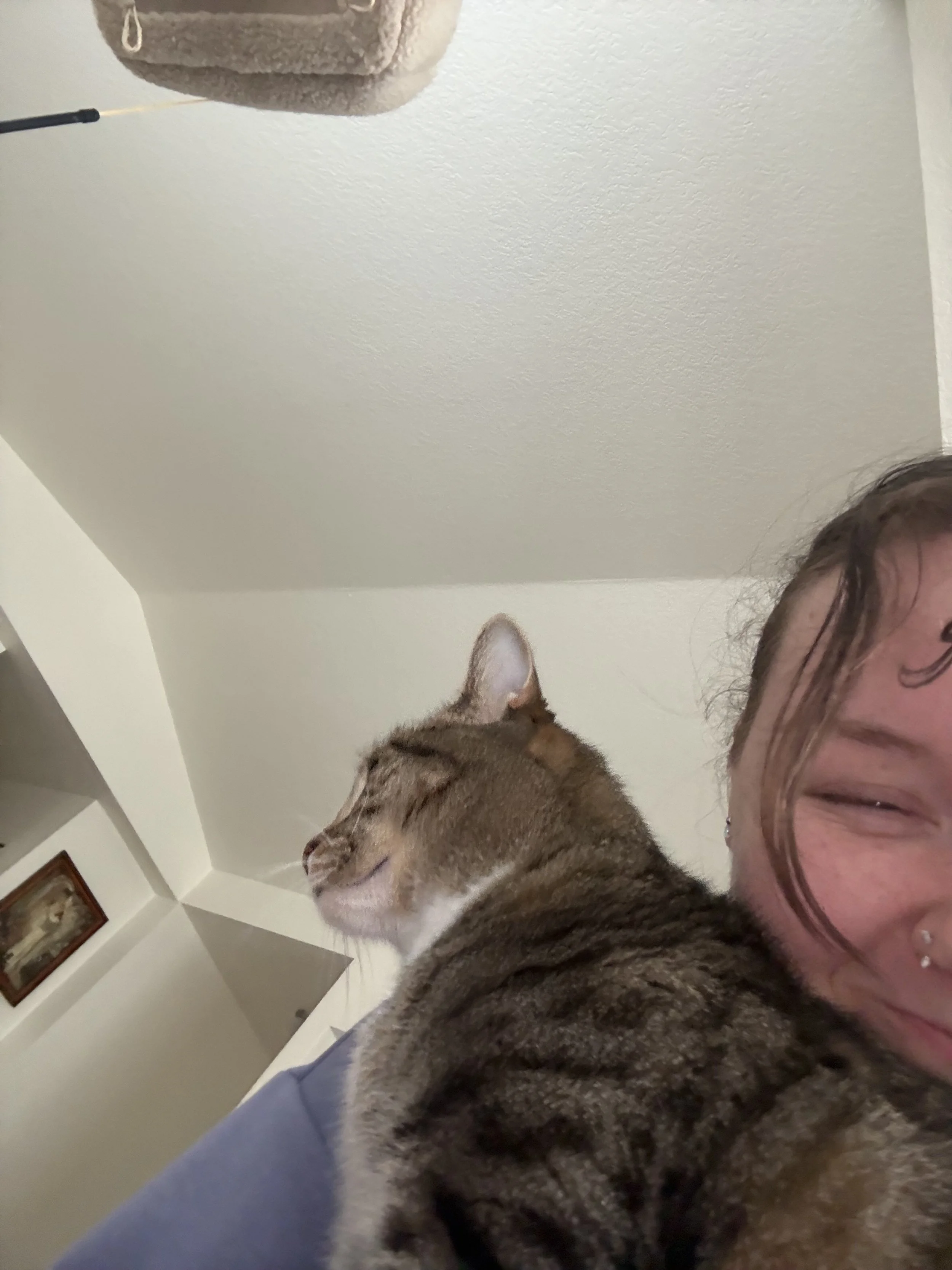 A girl half in the frame of the picture, smiling and posing next to a brown striped cat