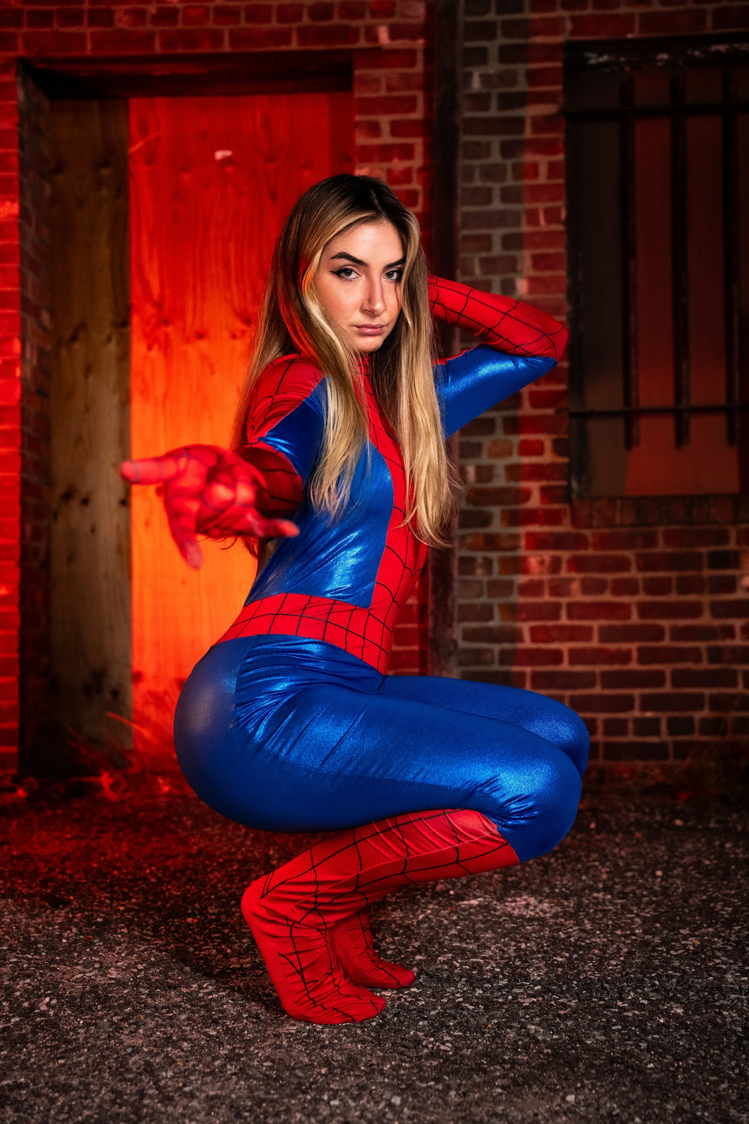 Lindsay dressed as Spider-Girl during a Halloween cosplay photography session against a red-lit brick wall in Patchogue, Long Island.