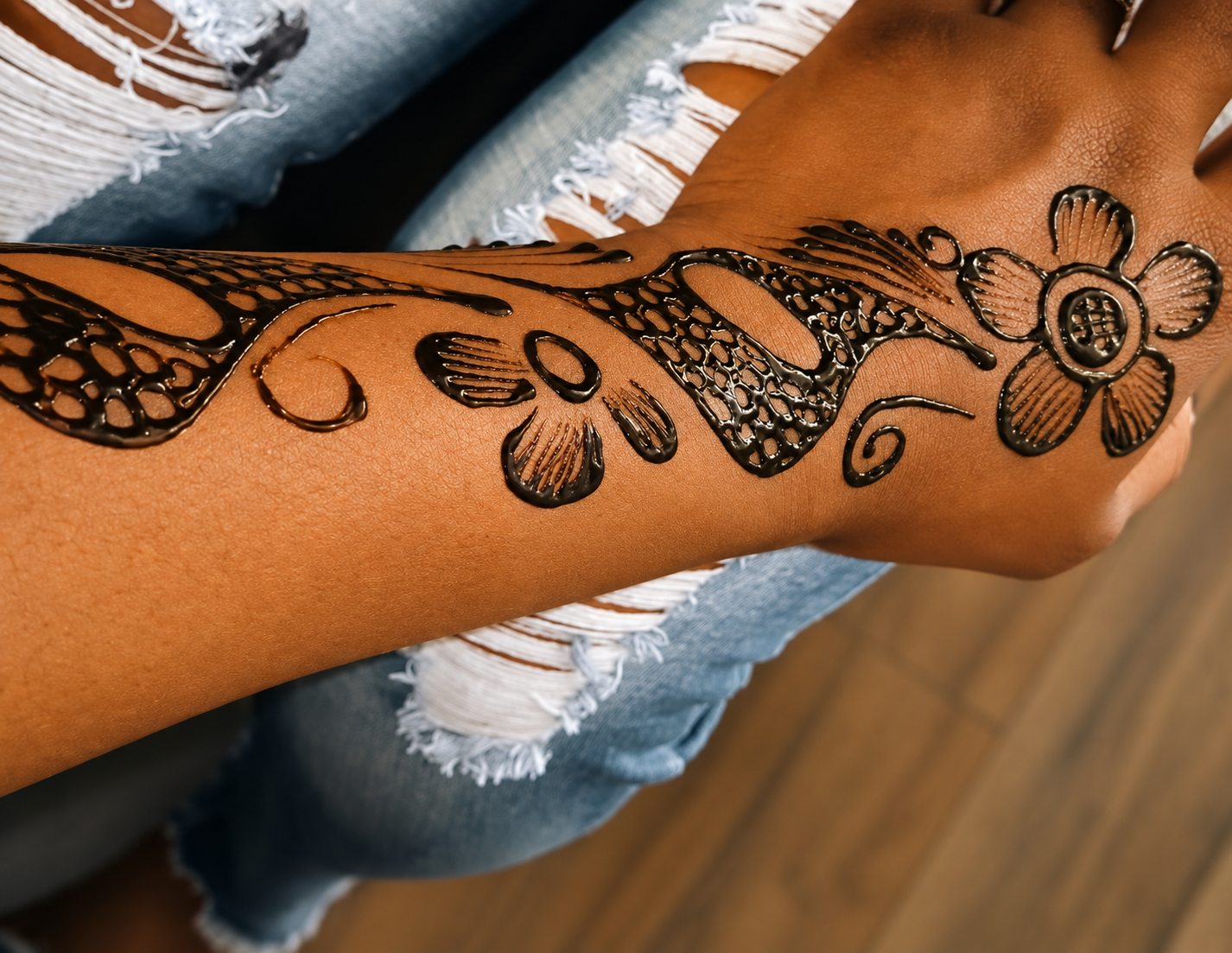 A person's arm with a black henna tattoo featuring a floral design.