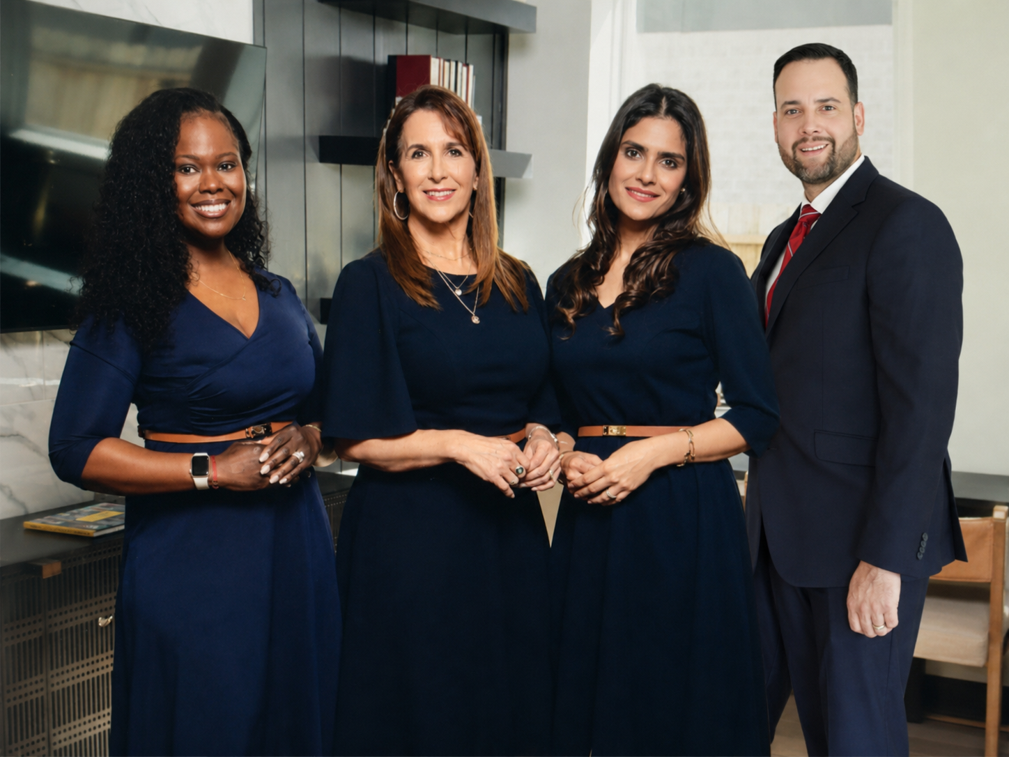 A diverse group of four professionally dressed people standing together indoors, smiling at the camera.
