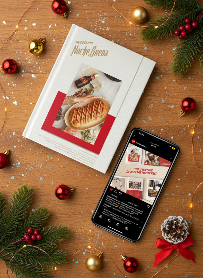 A cookbook titled 'Recetario Noche Buena' on a wooden table surrounded by Christmas decorations, including pine branches, red and gold ornaments, a pine cone, and confetti. A smartphone displaying a social media post about Christmas recipes is also on the table.