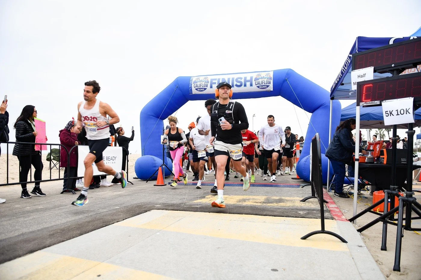 Runners crossing the finish line at a marathon with an inflatable blue arch, spectators, and race officials nearby.