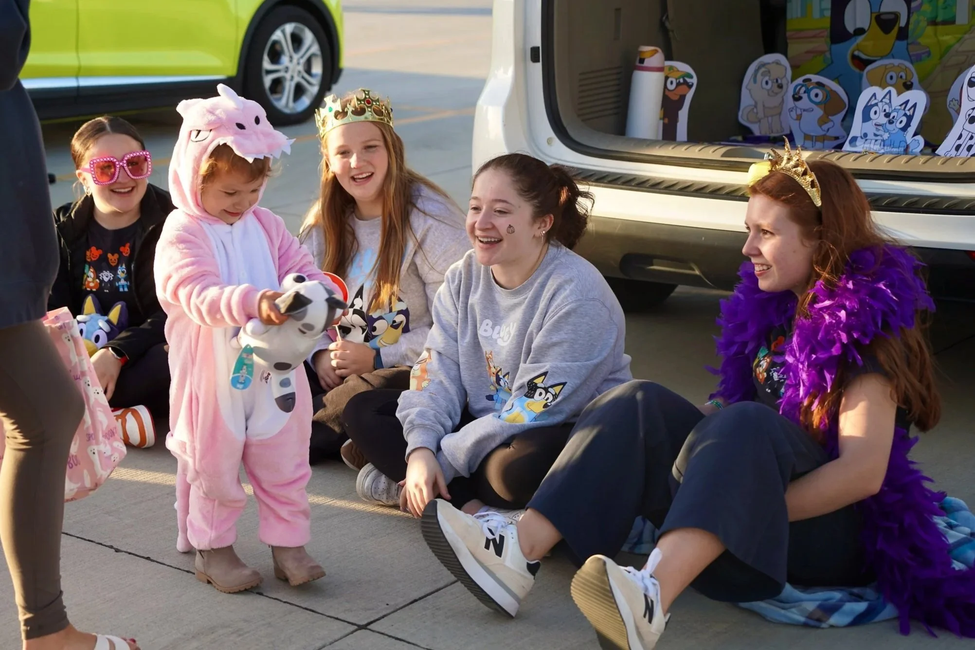 2024 - Surrounded by seniors Kaydence Meraz, Ayla Meraz and Alyssa Belitz, along with junior Ava Fink, a Trunk-or-Treater smiles at a "Muffin" stuffed animal on Oct 27. The girls' trunk theme was "Bluey," which the little girl loved. 