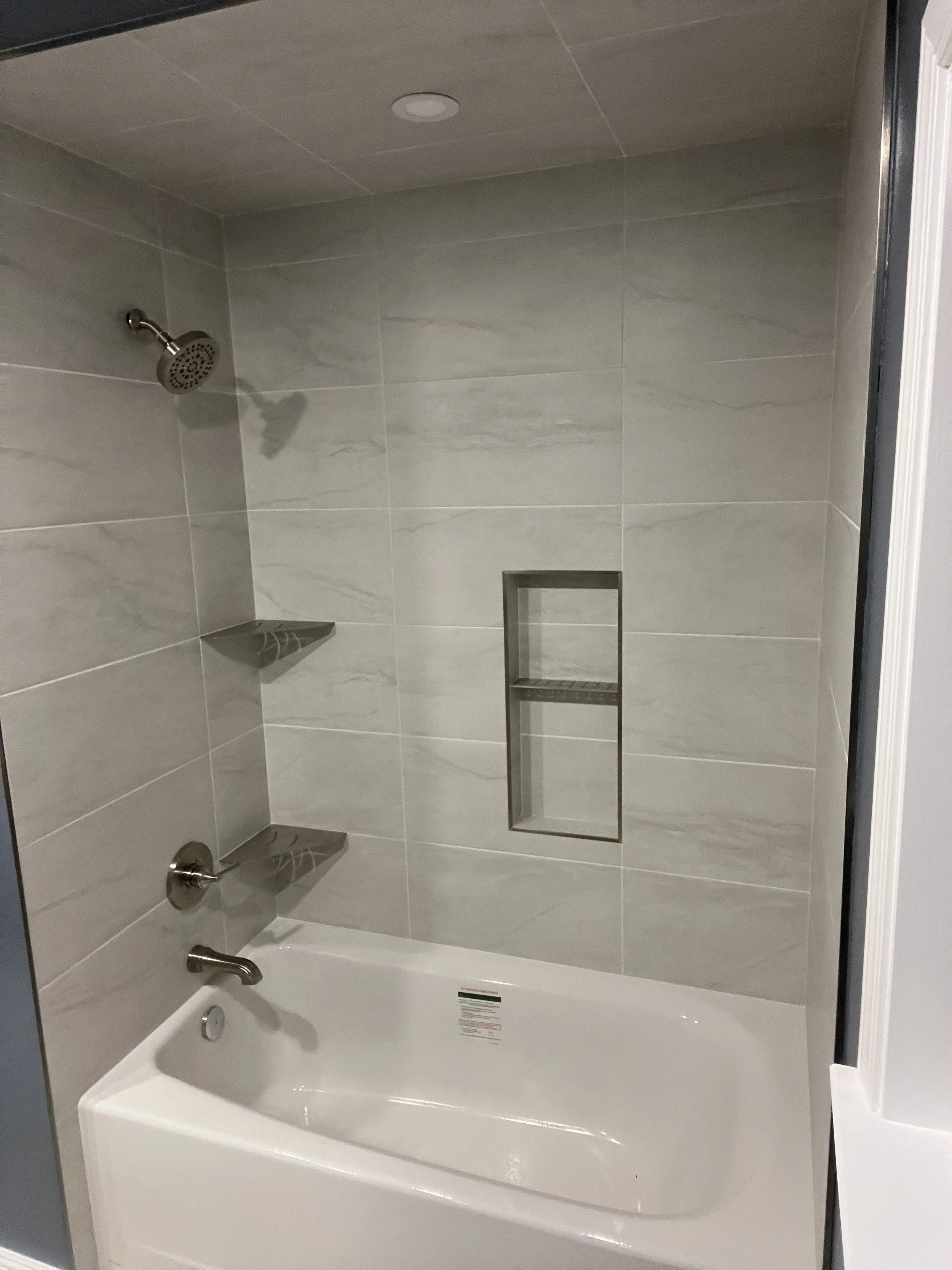 A shower area with beige marble tiles, a showerhead, a bathtub, and a built-in wall shelf.