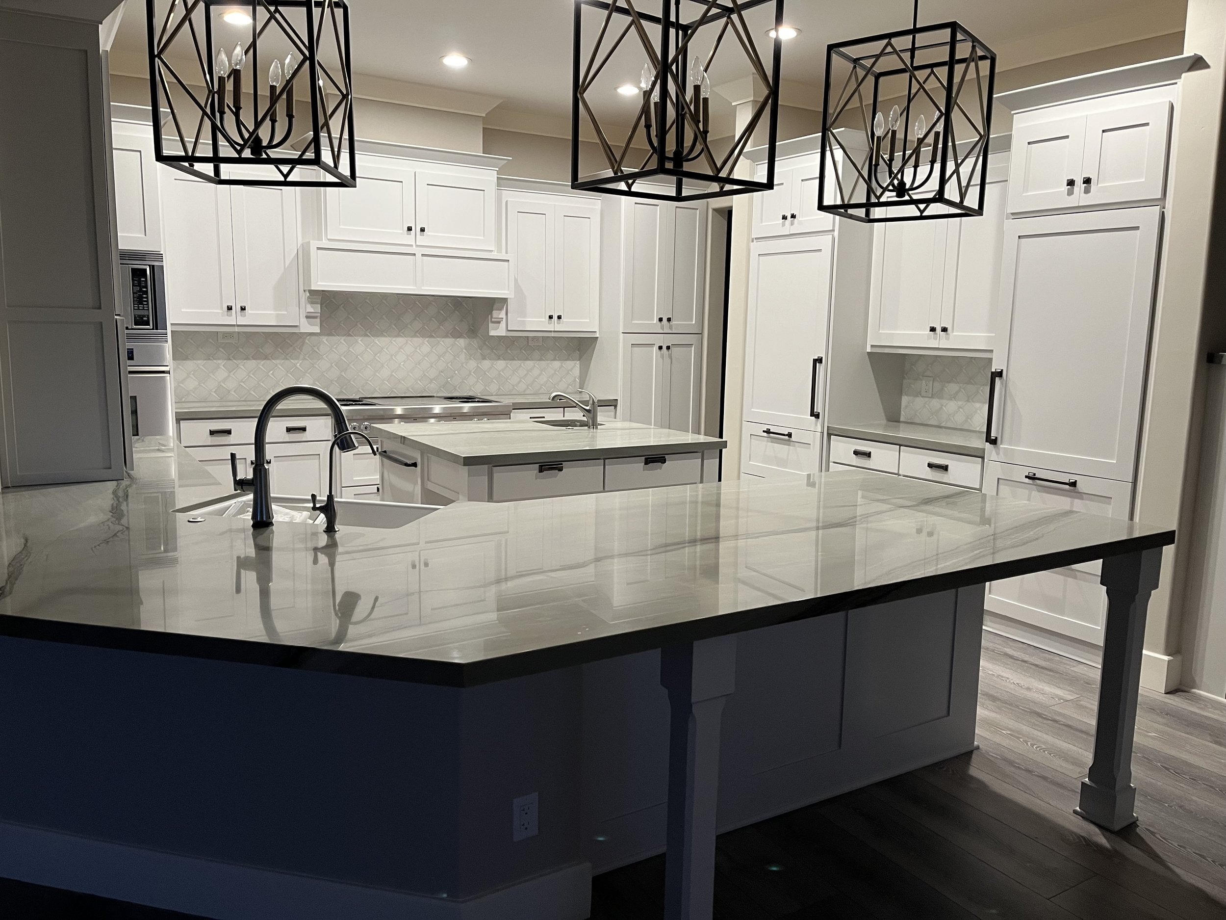 Modern kitchen with white cabinets, a large central island with a marble countertop, black pendant lights, and stainless steel appliances, including a built-in microwave and oven.