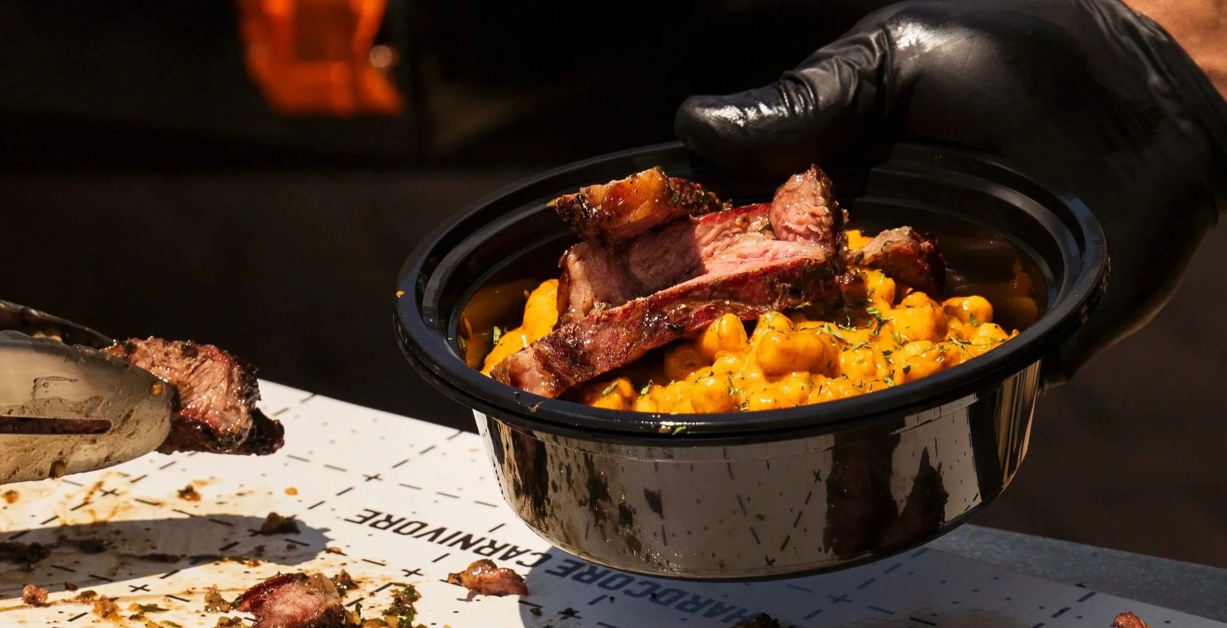 A slow cooker with cooked meat and yellow chickpeas garnished with herbs, being handled with a gloved hand.