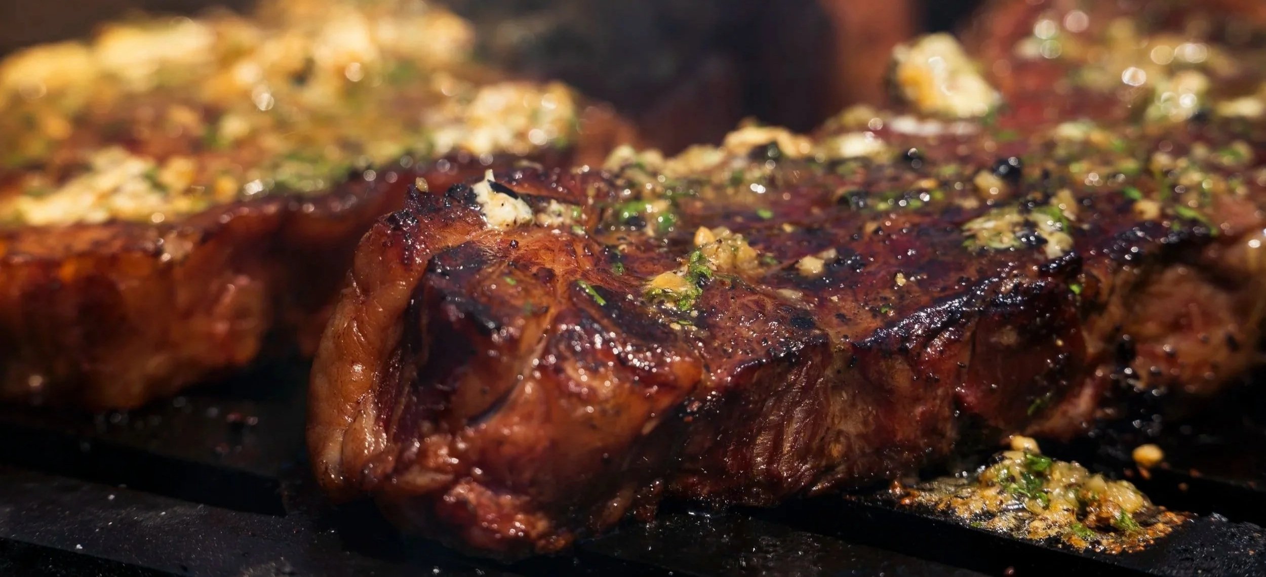 Close-up of a grilled meat steak topped with herbs and garlic, with a caramelized crust.