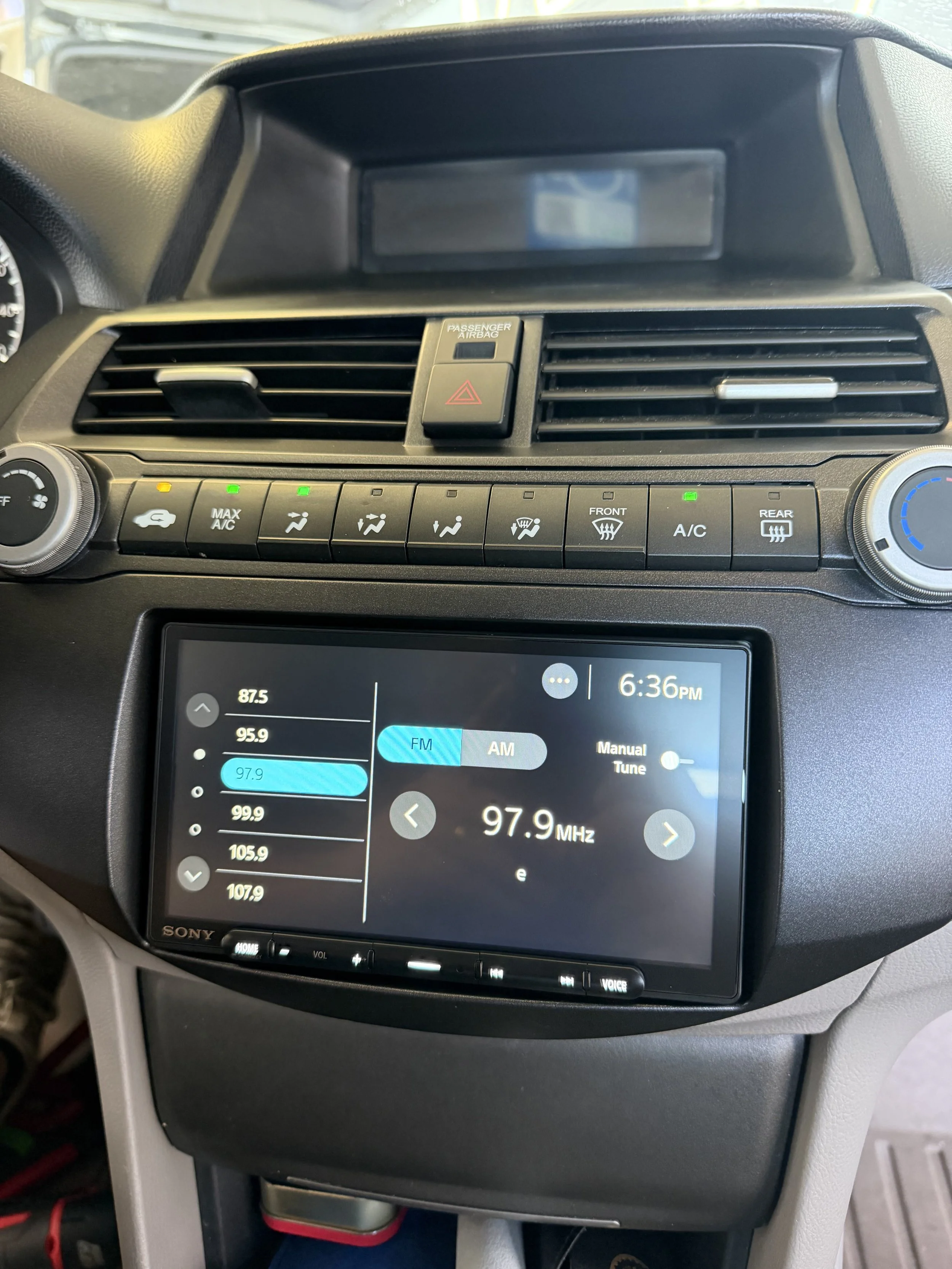 Car dashboard with radio display tuned to 97.9 FM, climate control buttons, and air vents.