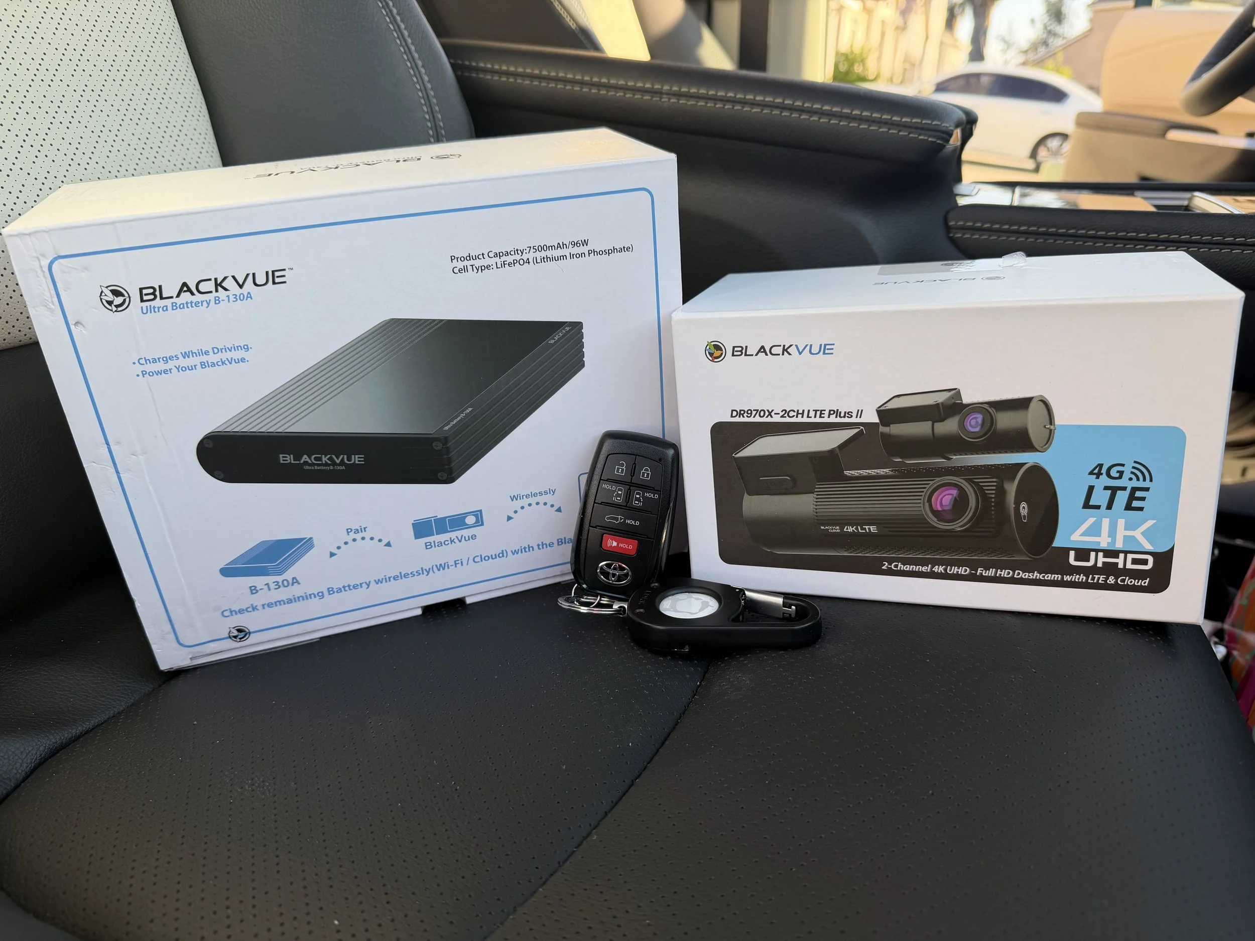 Car seat with two boxes of BlackVue electronic products, a car key fob, and a small remote control on the seat.