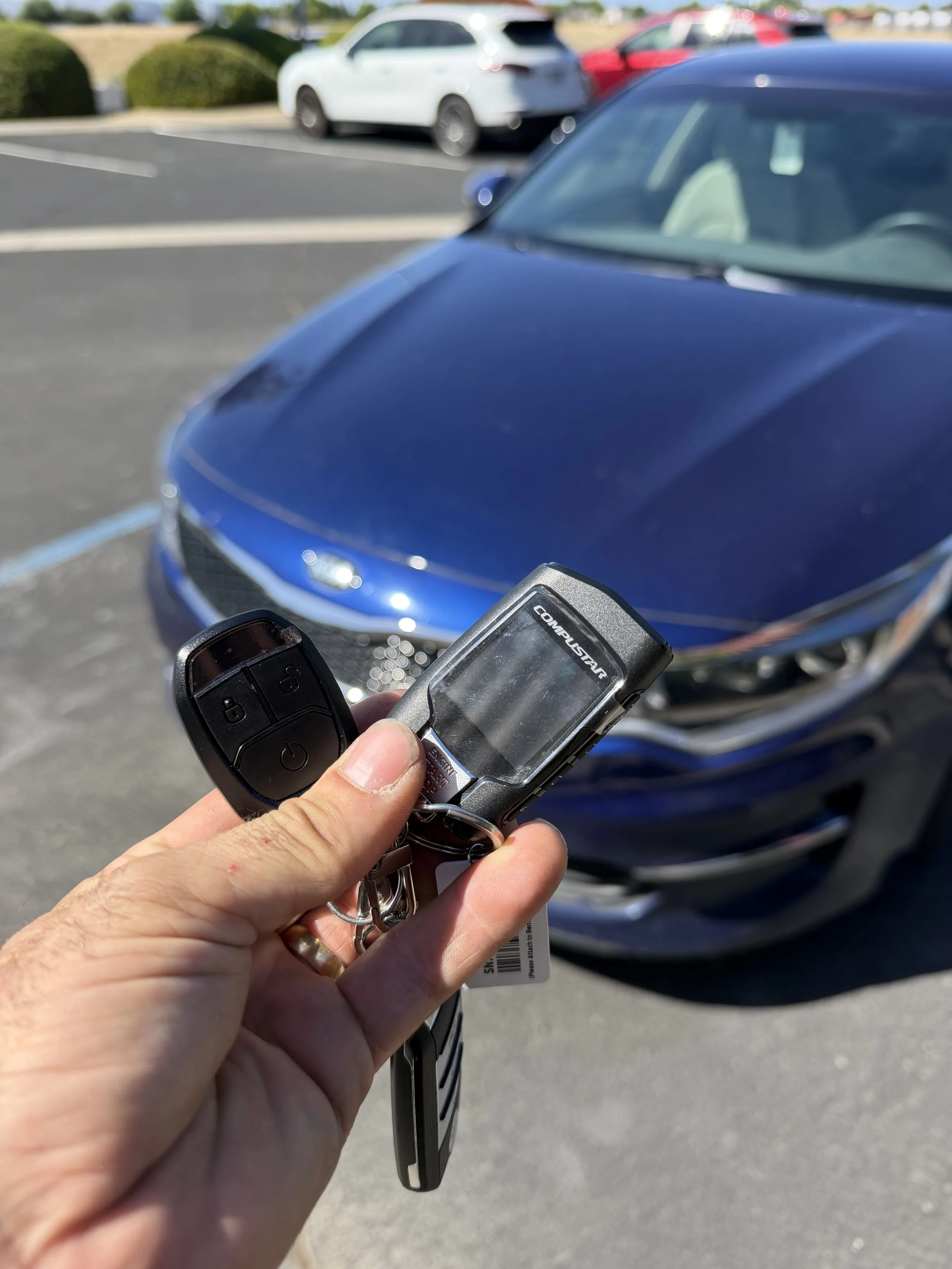 Hand holding car keys with a blue car in the background in a parking lot.