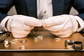 Person wearing white gloves handling rings on a desk with more rings and a magnifying glass.