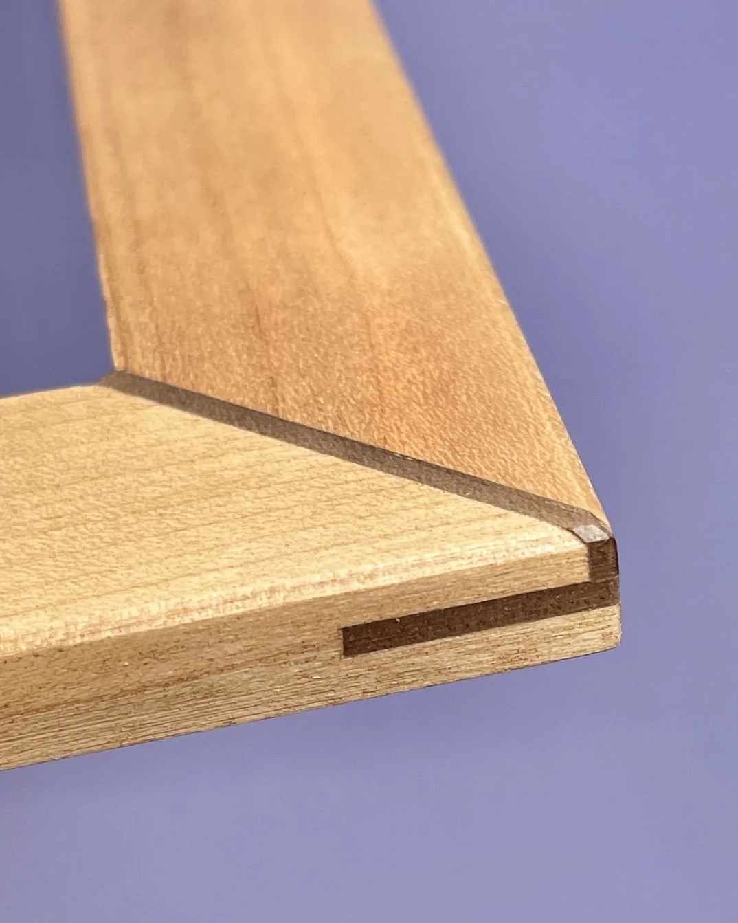 Detail eines Kirschholzdeckels (Show+Case-Rahmen) mit Nussbaum-Eckenverstärkung vor lila Hintergrund.