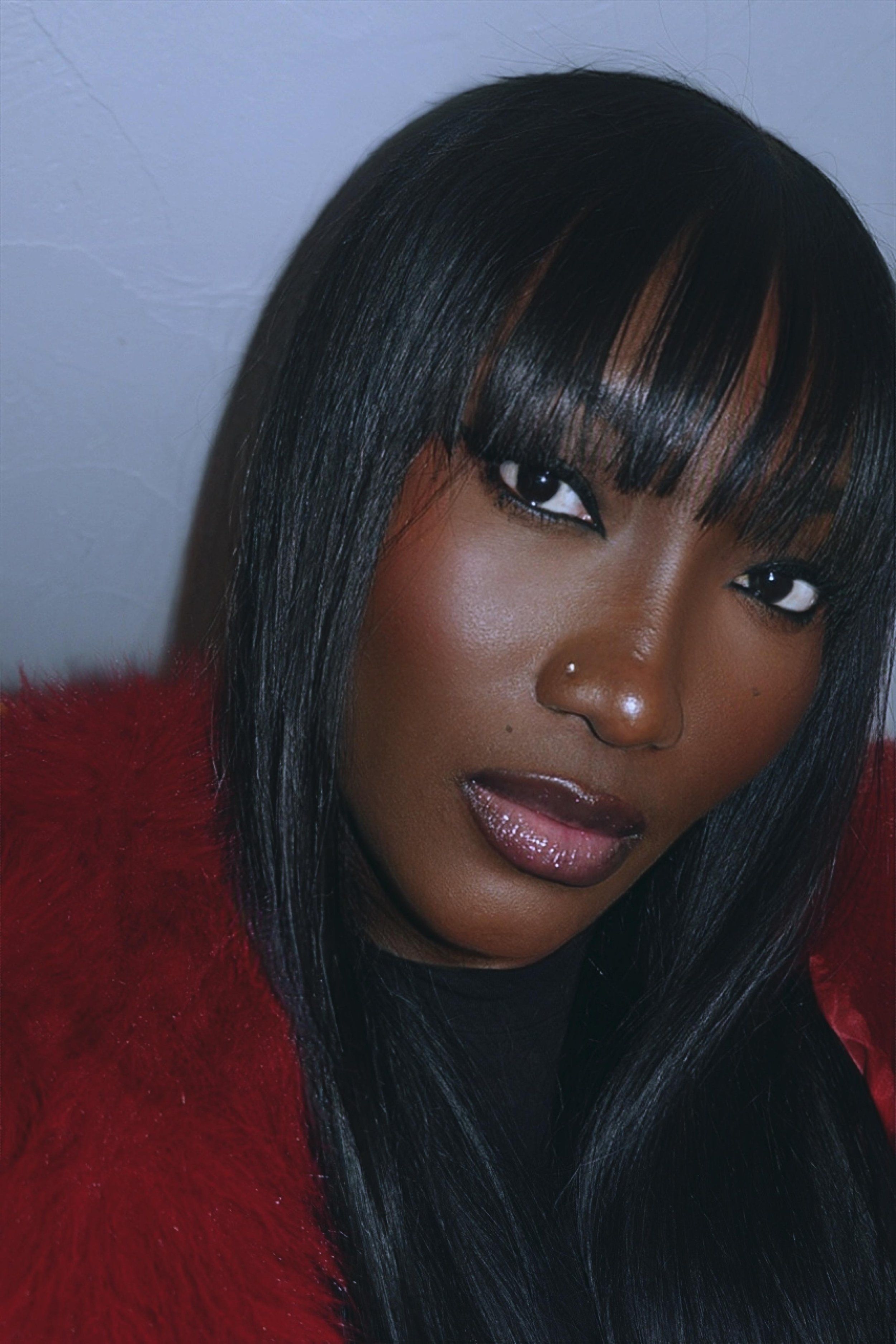 Close-up of a woman with straight black hair and bangs, wearing a red fuzzy coat, and looking at the camera.