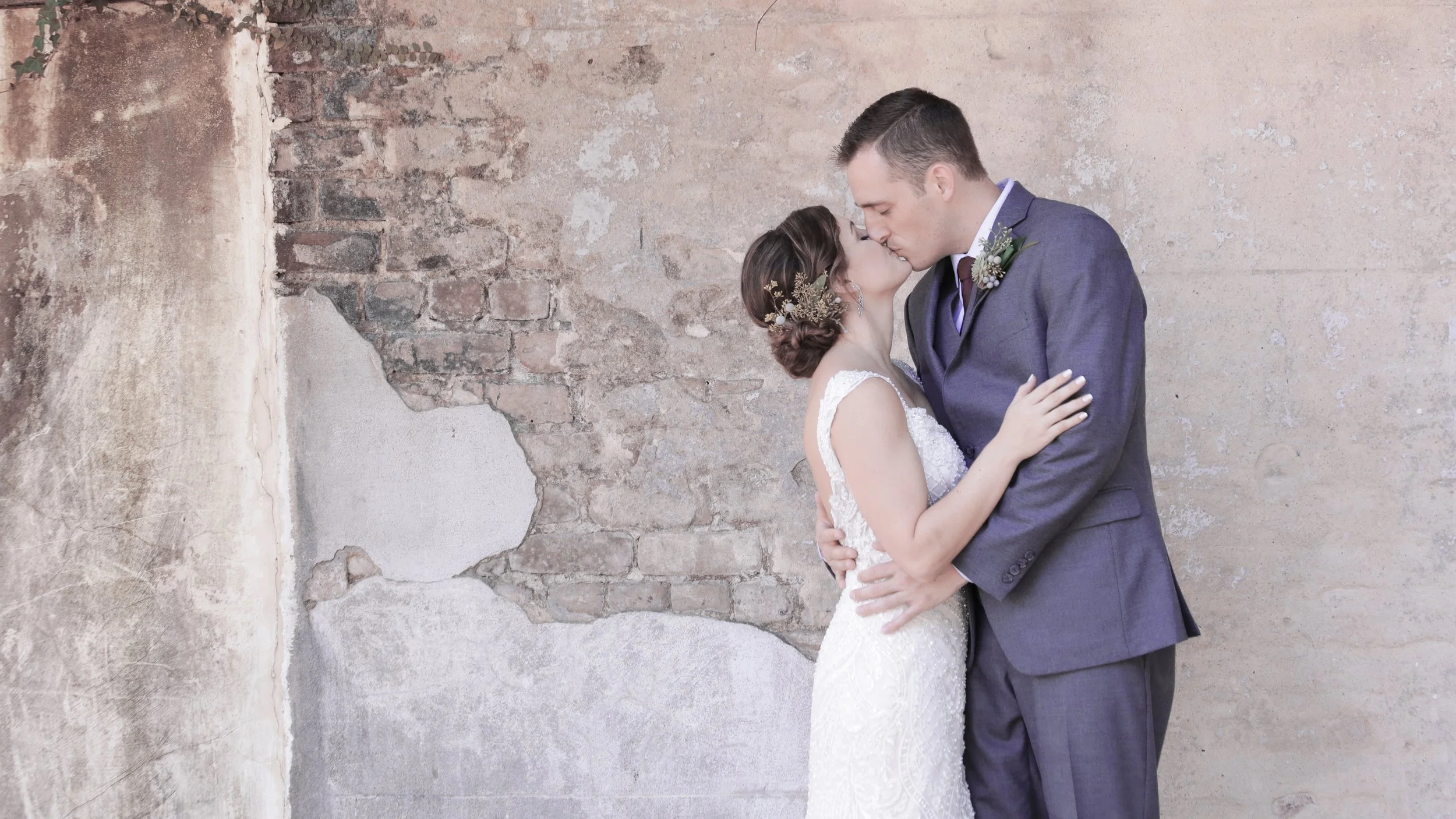 Charlie & Melanie embrace and kiss before a rustic wall  in historic Savannah, Georgia.