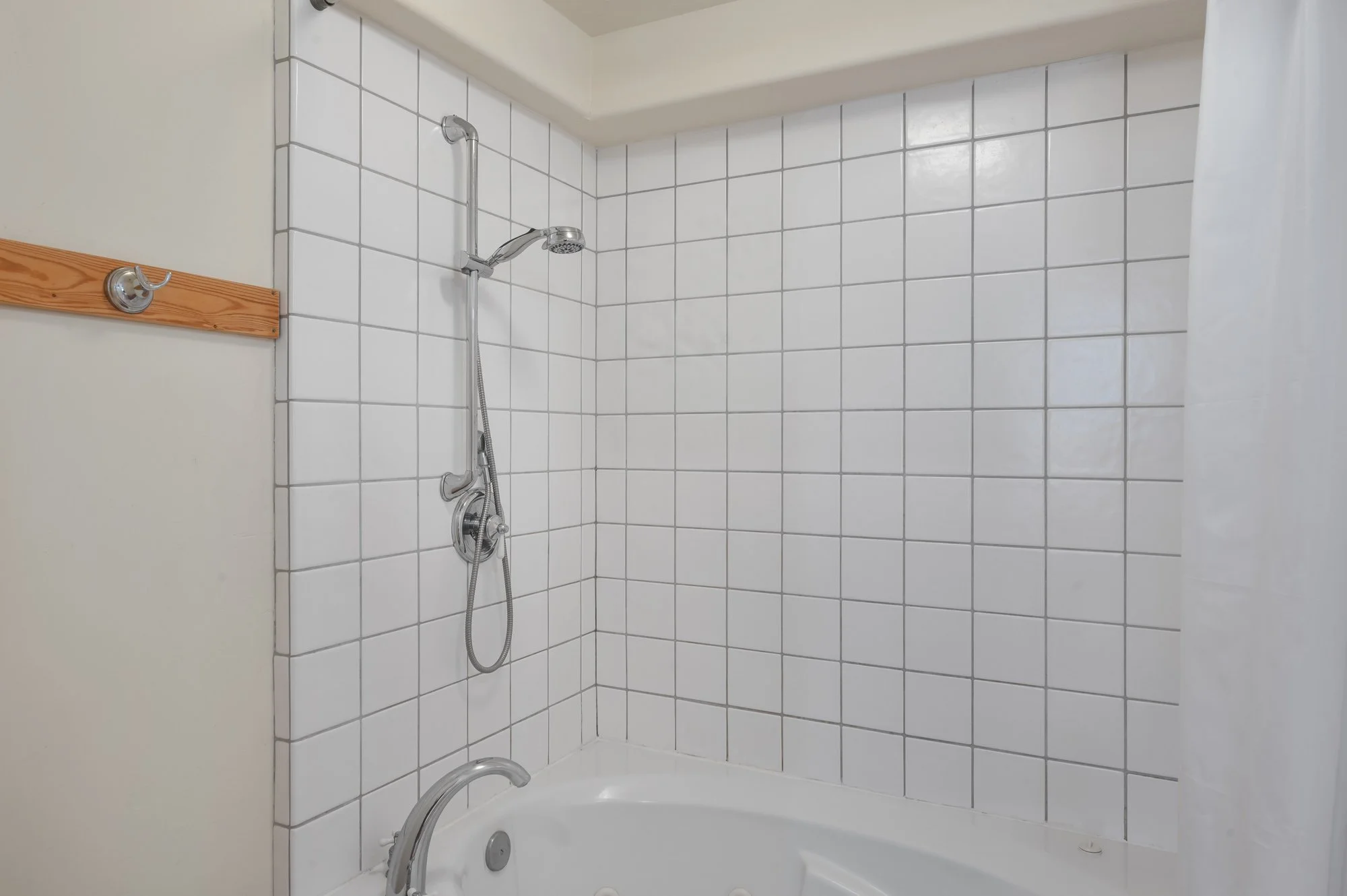 Bathroom shower with white tiled walls, a silver showerhead on a vertical rail, a handheld shower attachment, and a white bathtub.
