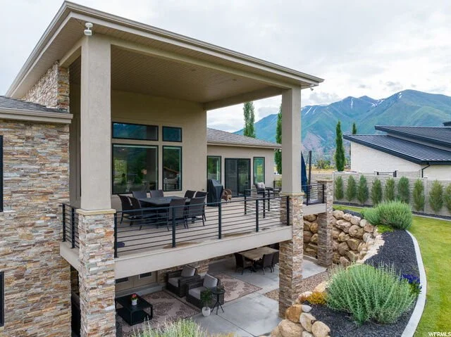 Outdoor balcony of a modern house with patio furniture, overlooking a landscaped yard with mountains in the background.