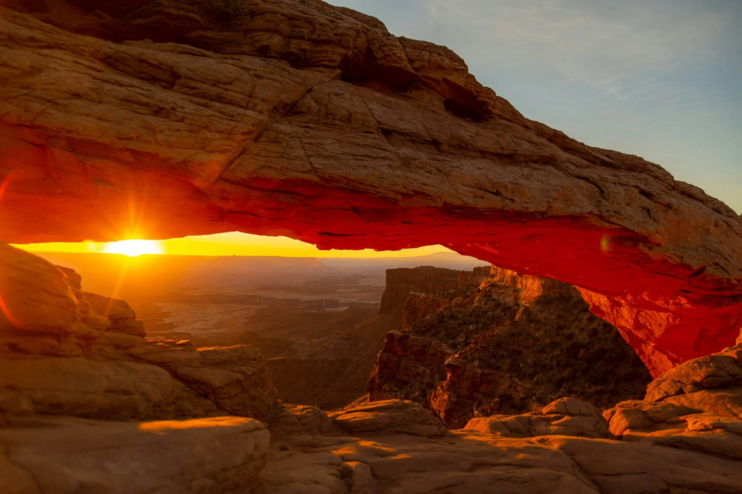 Sunset over a desert landscape viewed through a natural rock arch formation.