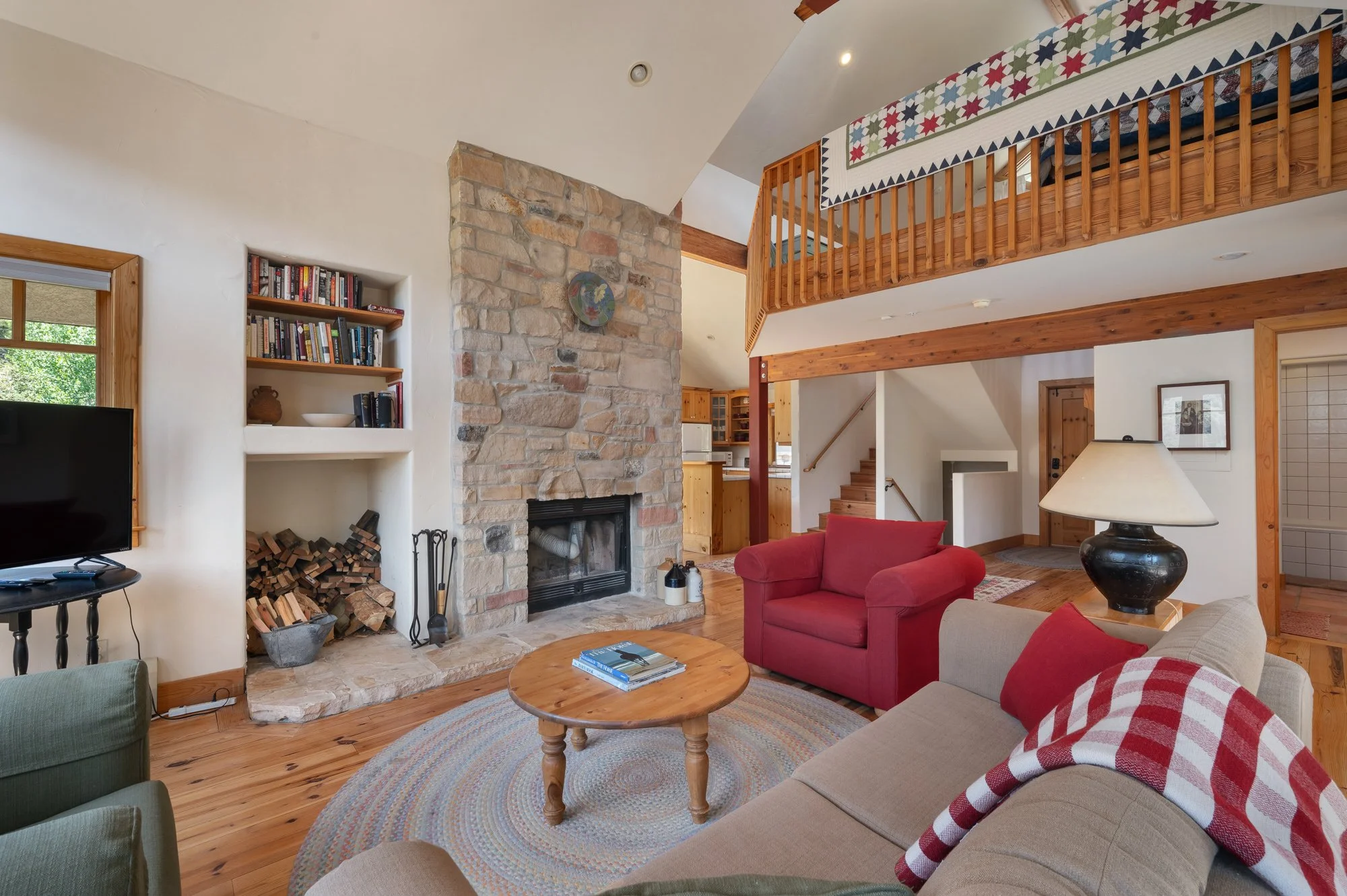 Living room with stone fireplace, wooden furniture, and seating area with red and beige chairs, and a coffee table, in a cozy home interior.