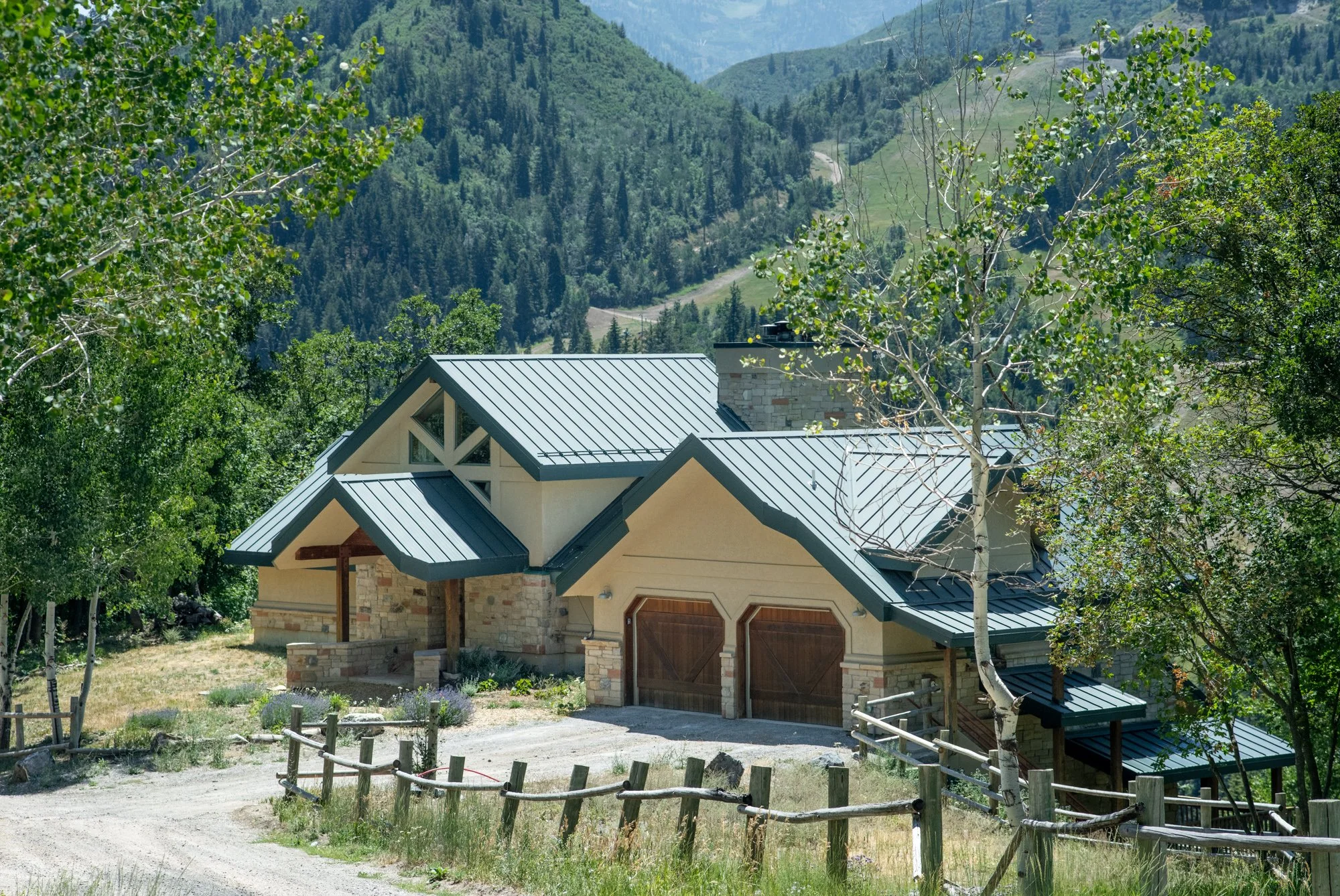 A house with a metal roof and stone accents situated in a wooded mountain area.