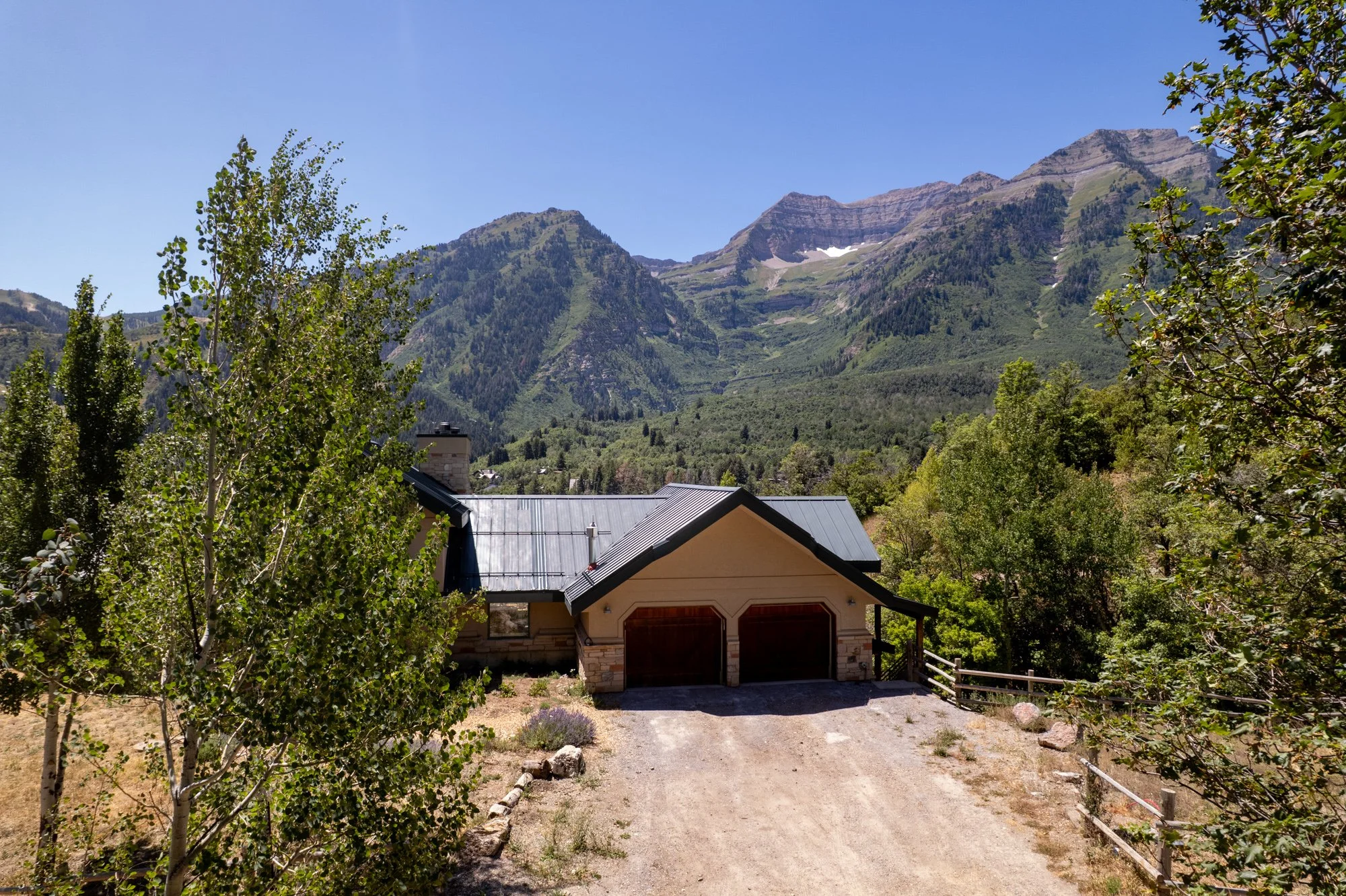 House with a metal roof in front of a mountain range with green slopes and a clear blue sky.