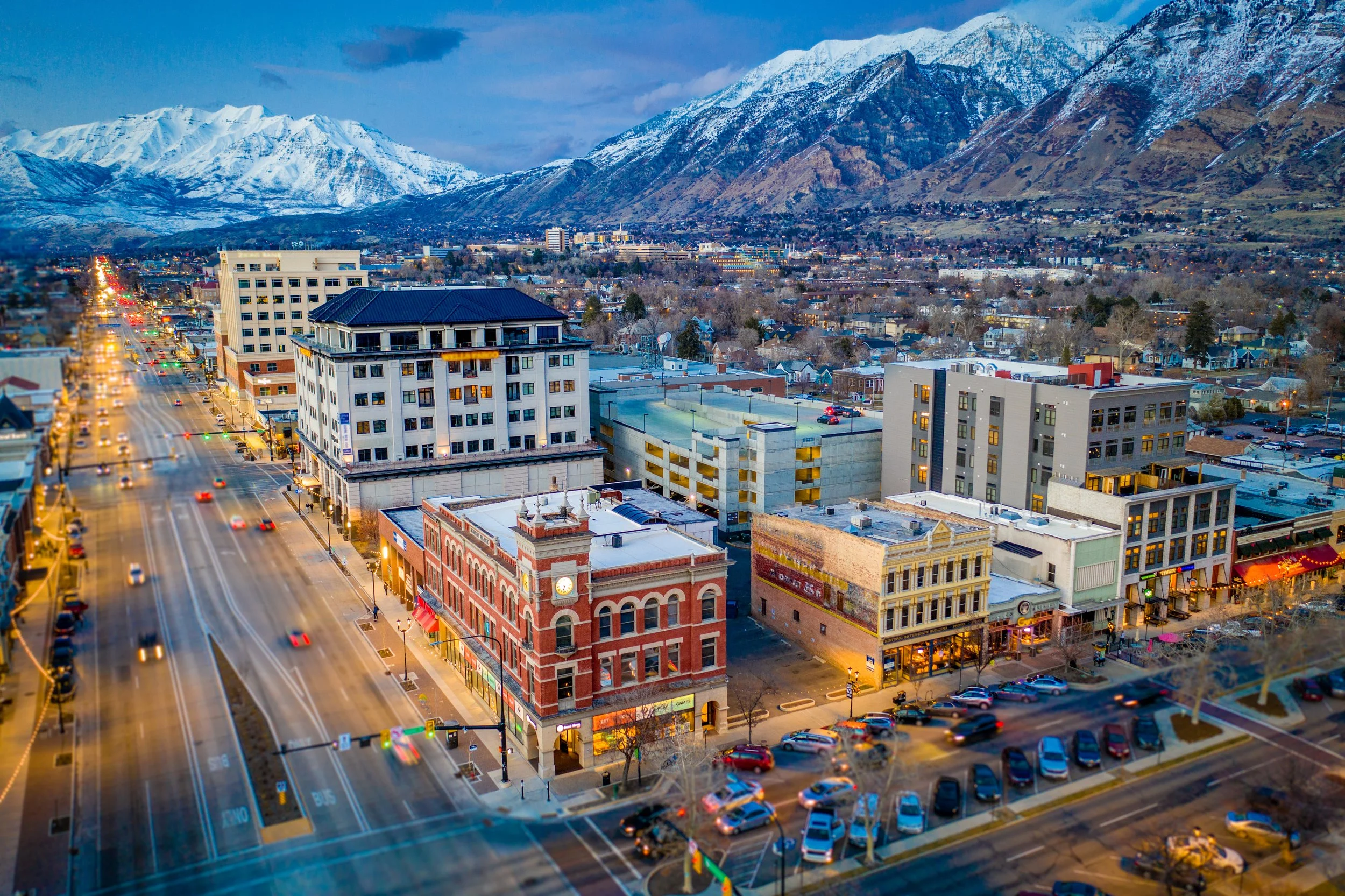 City street view overlooking downtown with buildings, cars, and mountains in the background at dusk.