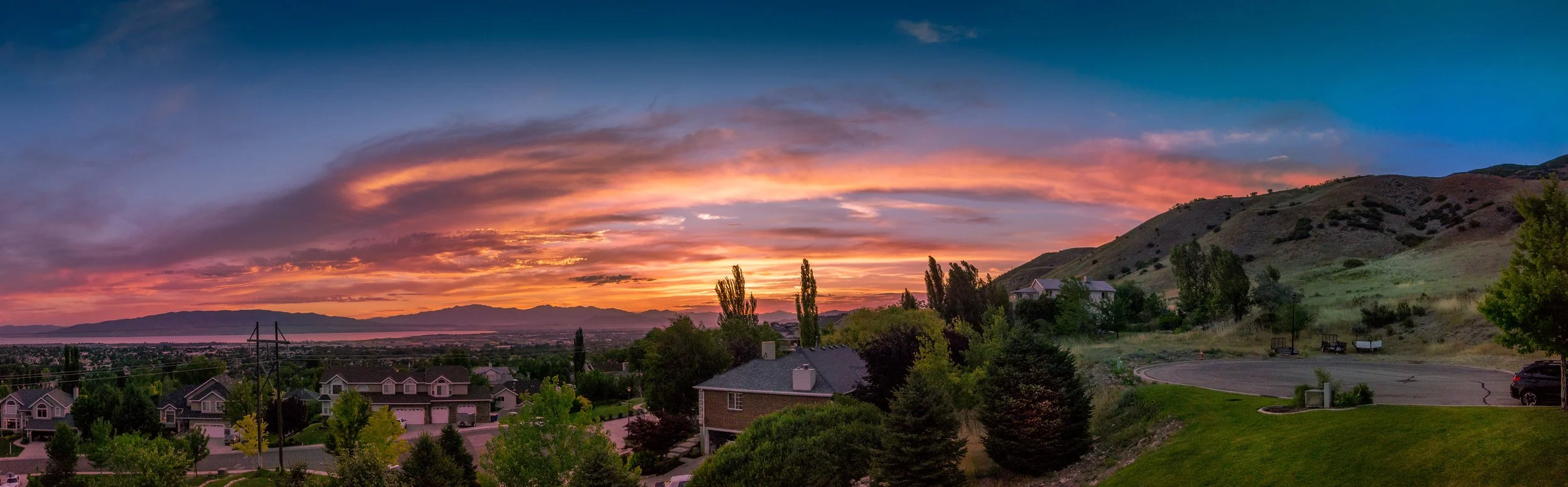 Sunset over a suburban neighborhood with houses, trees, and hills in the background.