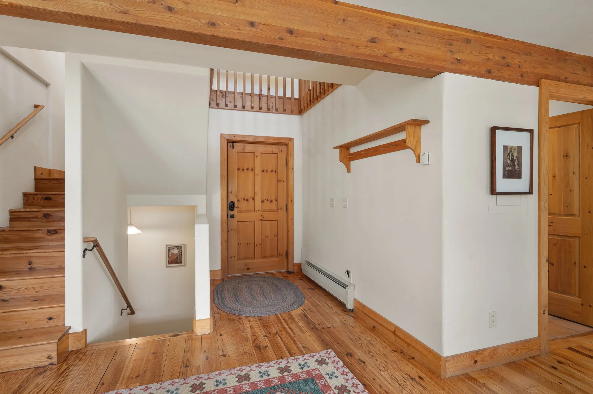 Interior view of a house entryway with wooden flooring, front door, staircase, and wood accents.