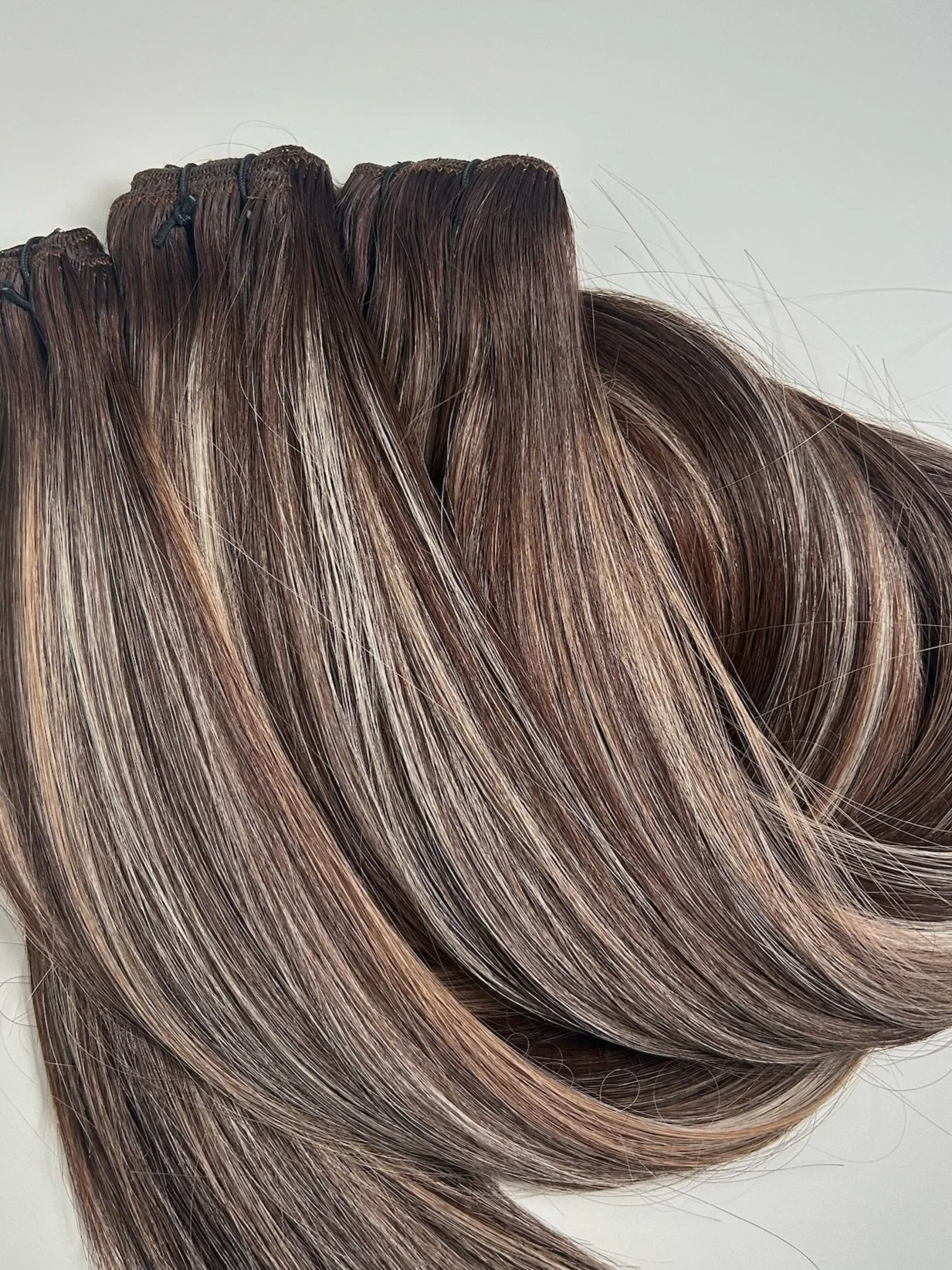 Multiple hair wefts with brown and blonde highlights on a white background.