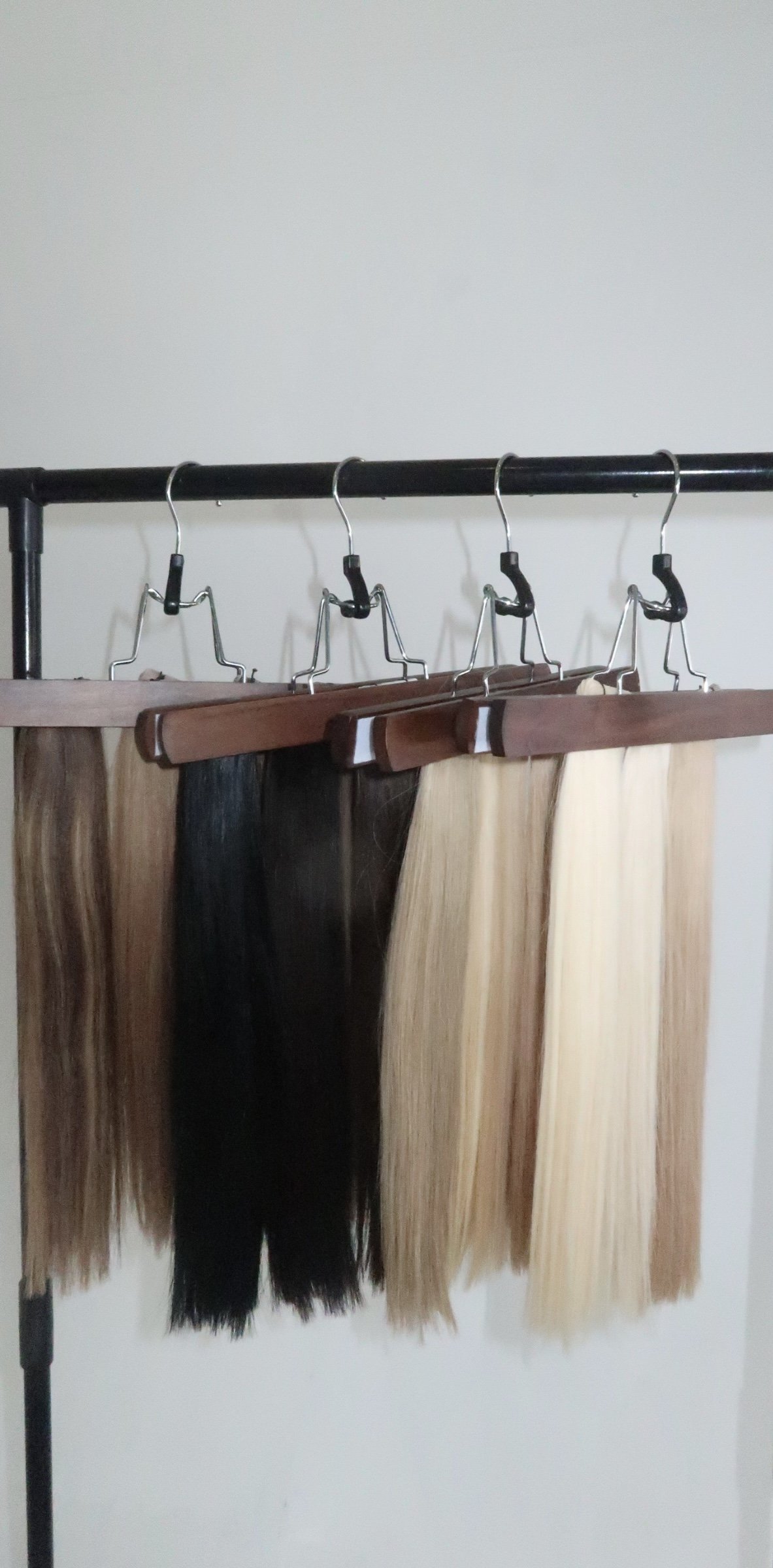 Four different hair color swatches hanging on hangers on a black clothing rack, displaying brown, black, light brown, and blonde hair extensions or samples.