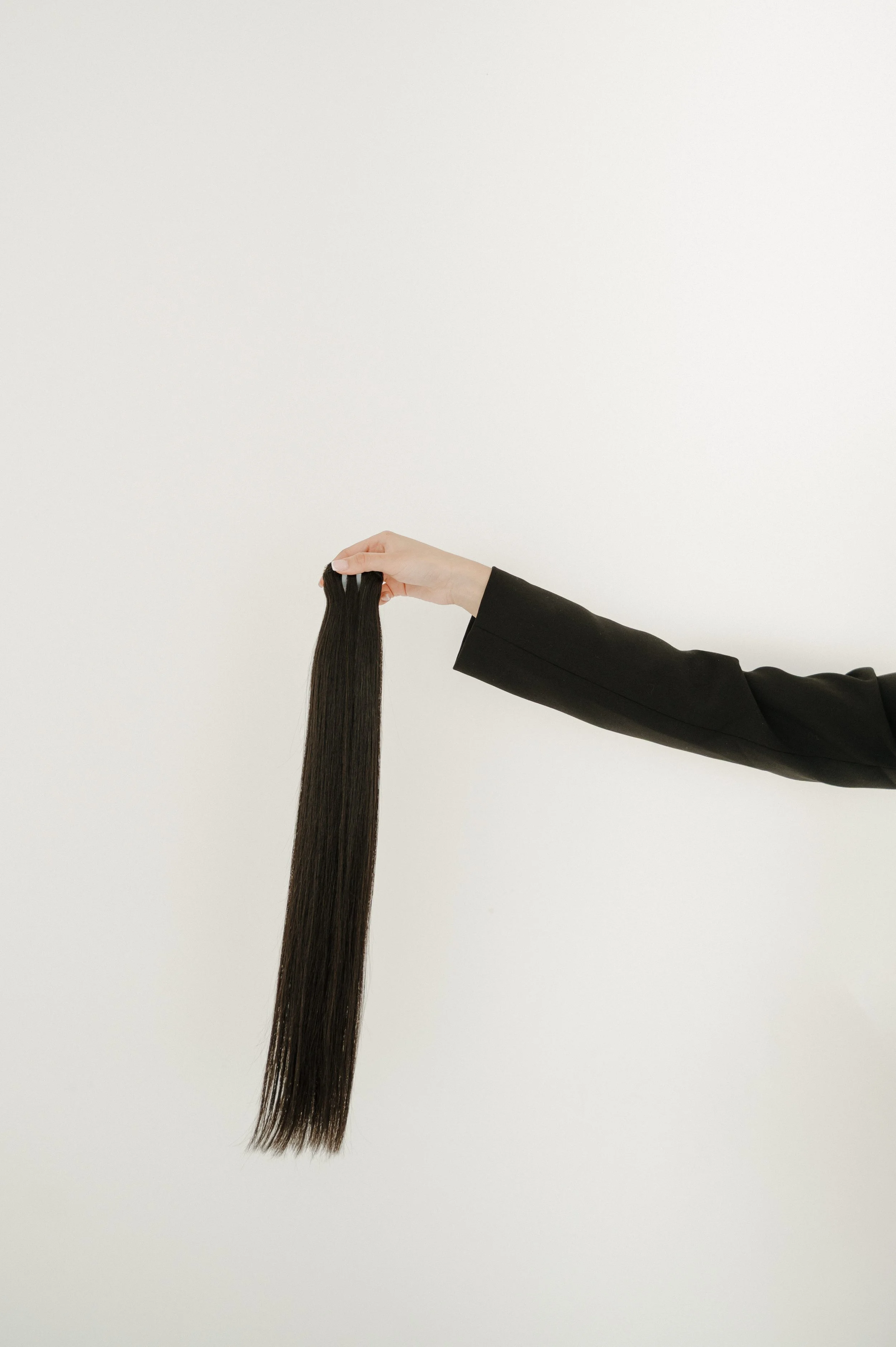 A person holding a long, straight, dark brown hair extension against a plain white background.