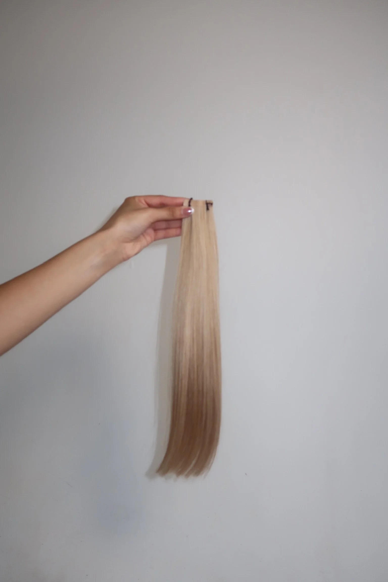 Hand holding a lock of blonde hair against a plain white wall.