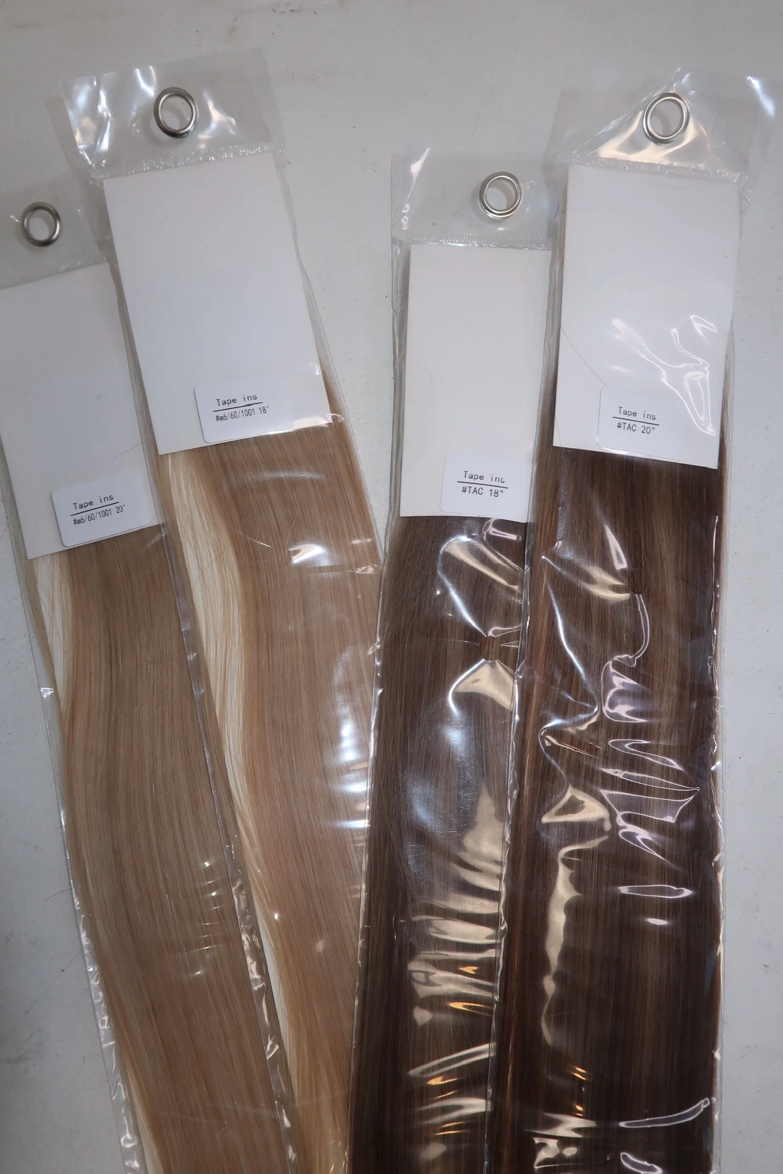 Four packs of hair extension samples in plastic packaging, labeled with different lengths and shades, placed on a white surface.