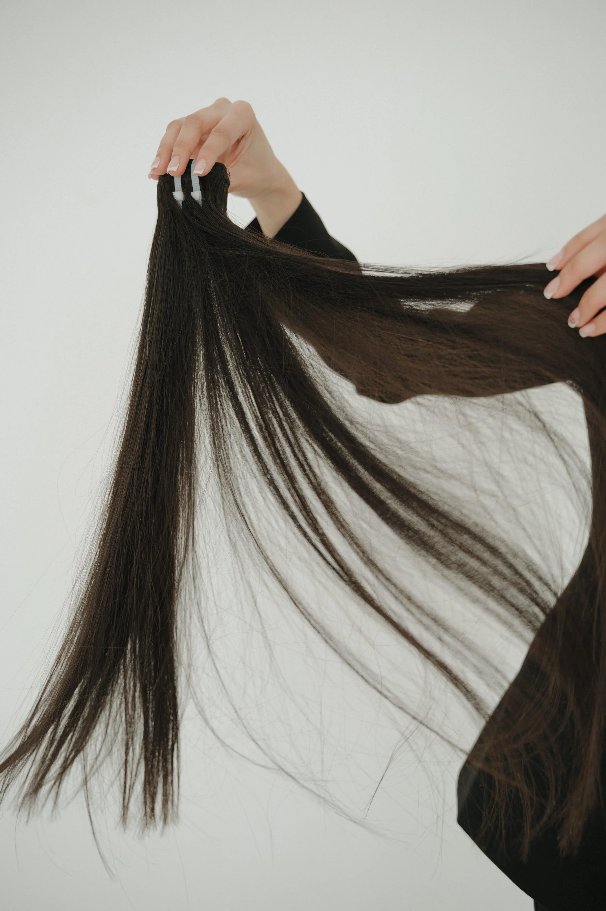 A person with long, straight brown hair, holding a small section of hair with their hand.