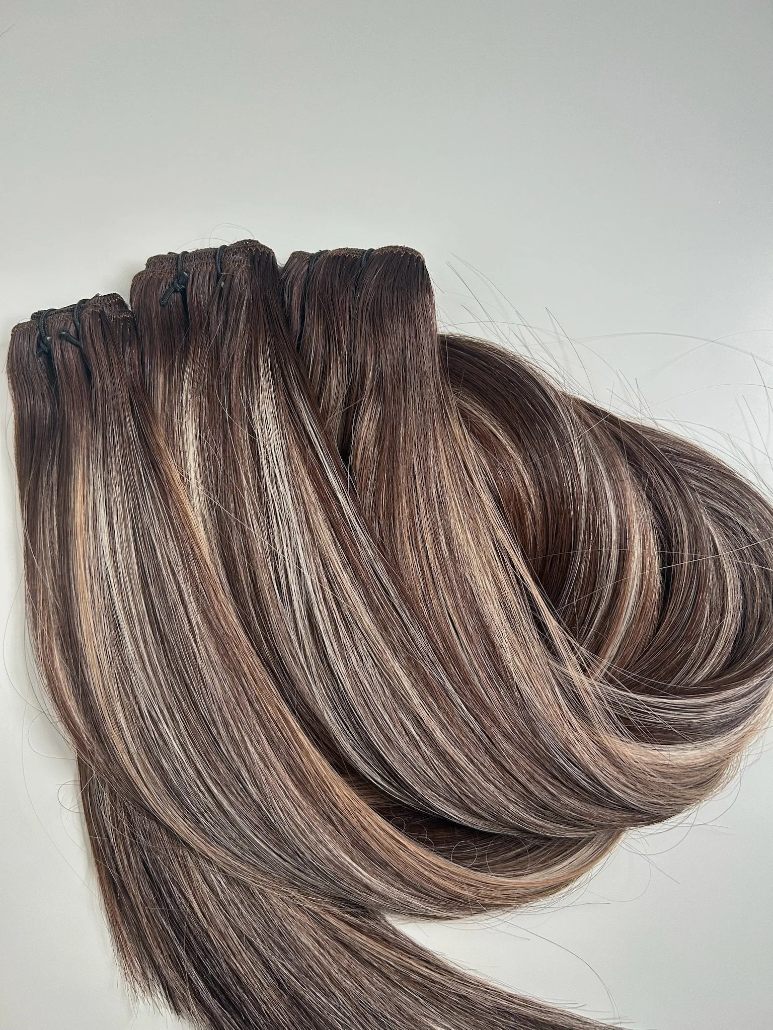 A bundle of brown, blonde, and light brown hair extensions with clips attached at the top.