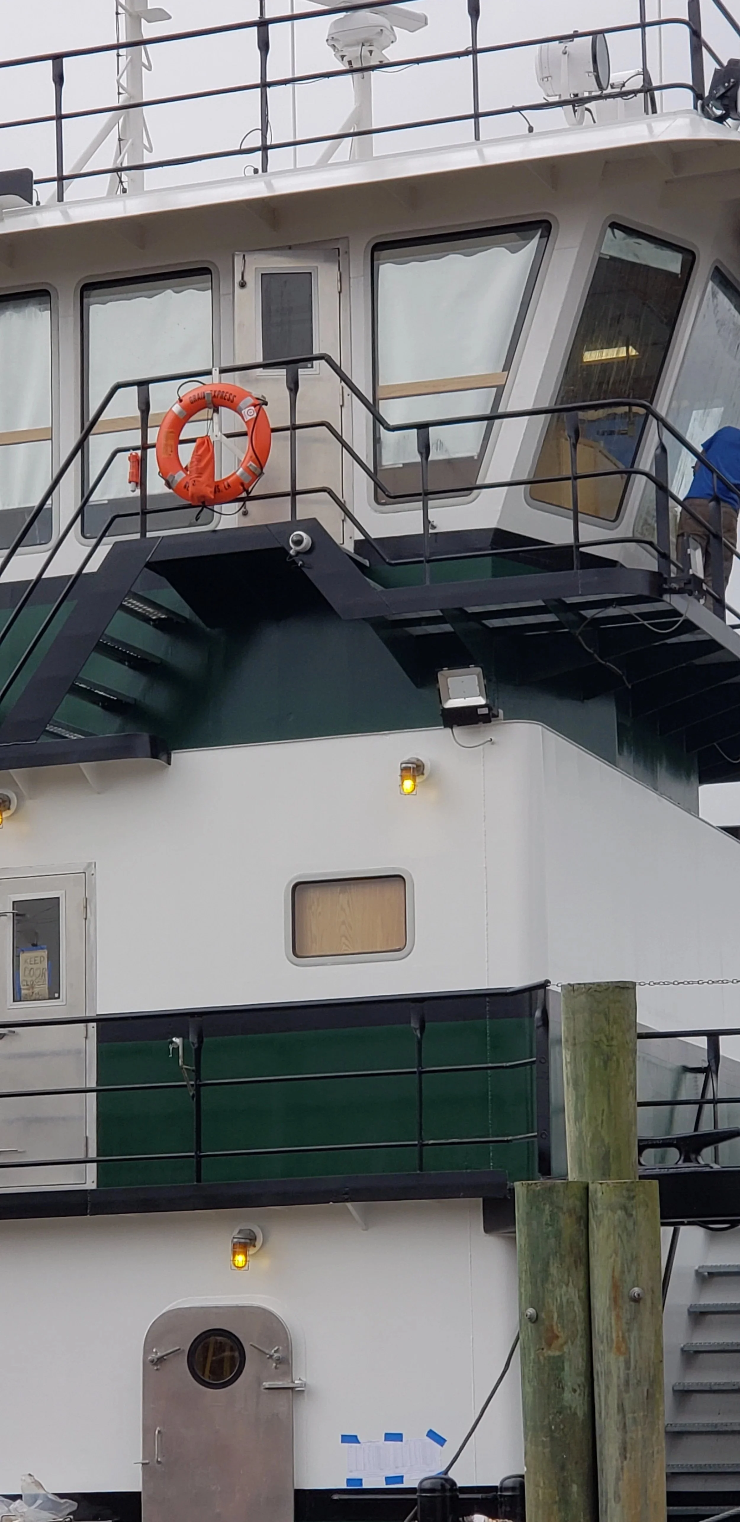 Close-up of a ship's bridge with navigation equipment, an orange life ring, and windows.