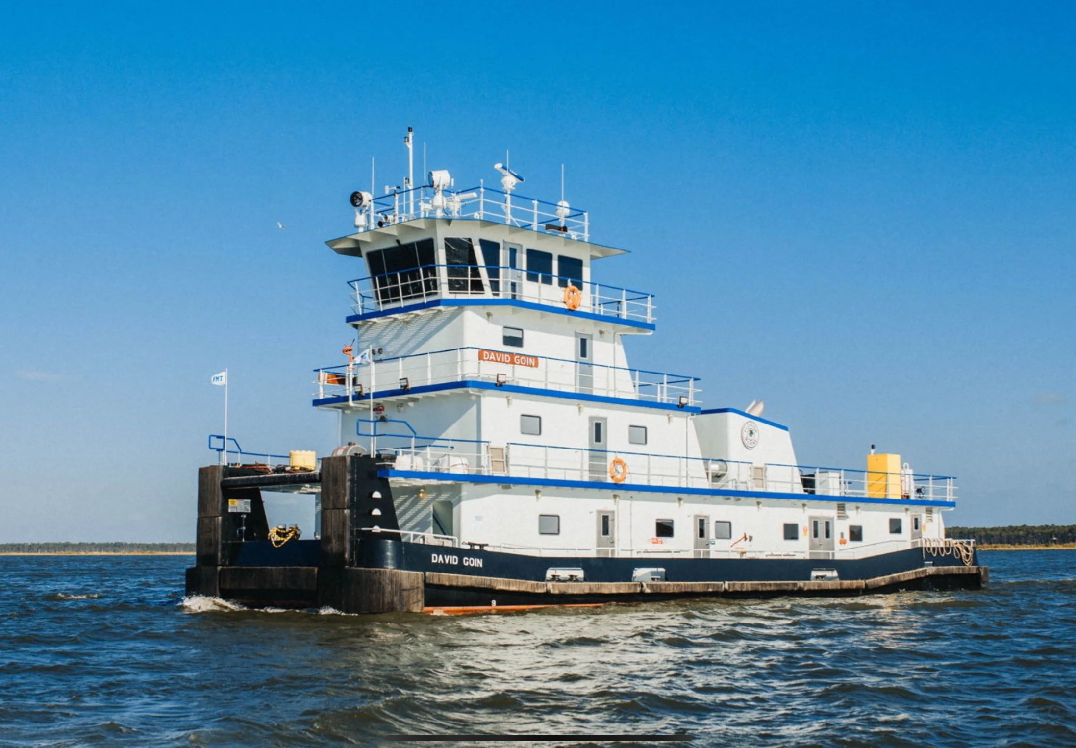 A large white tugboat named David Goin sailing on water with a clear blue sky in the background.
