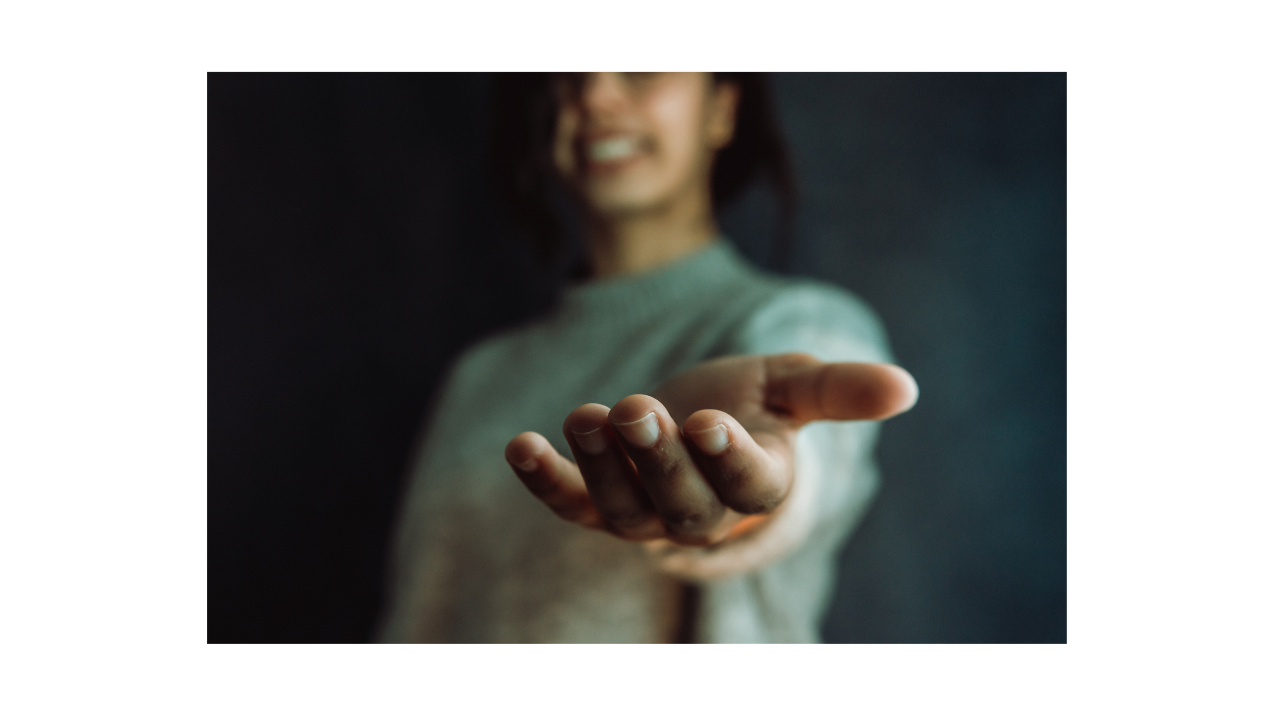 A person reaching out with their hand, smiling, with a blurred background.