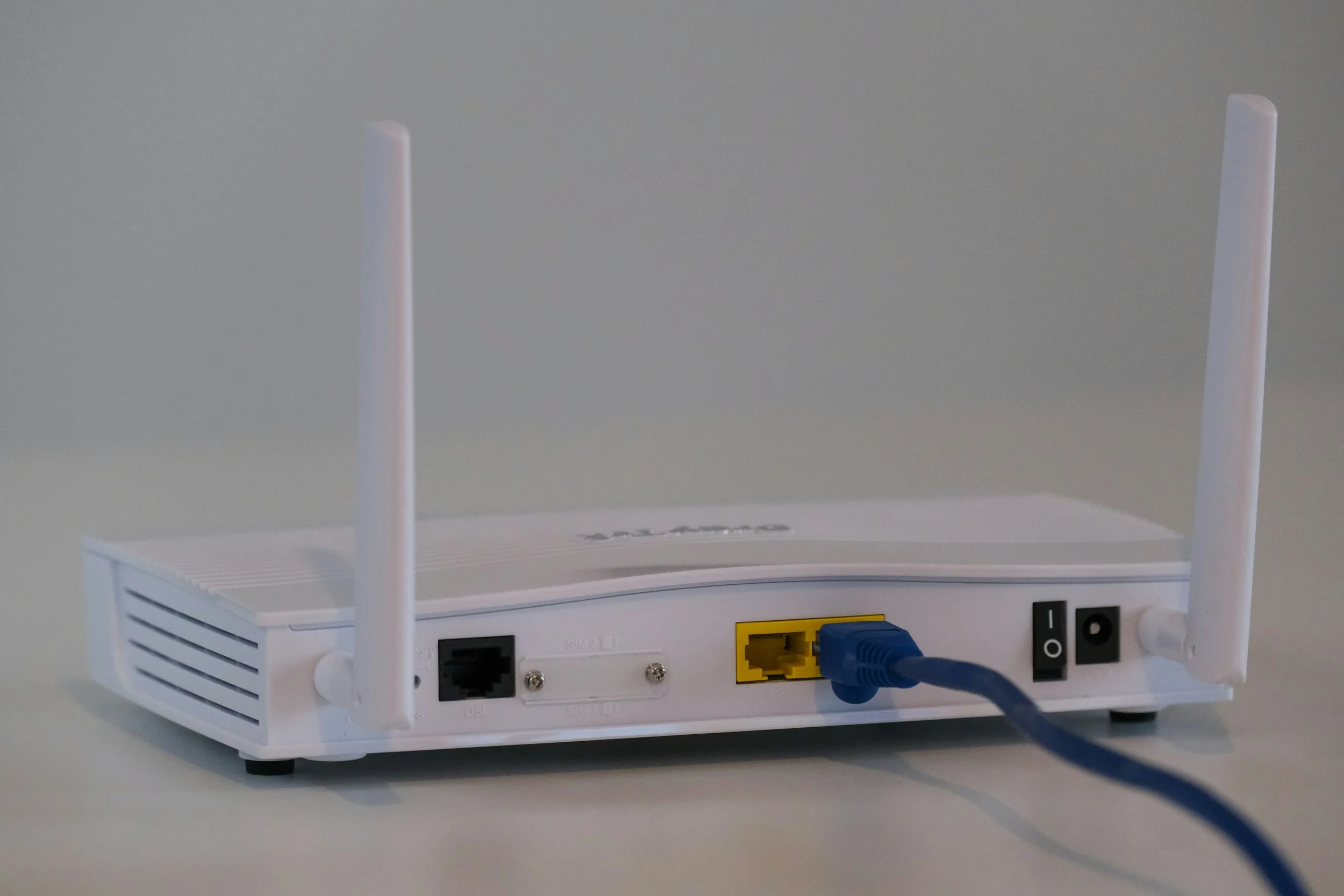 Wireless router with two antennas, connected to a blue Ethernet cable, on a white surface.