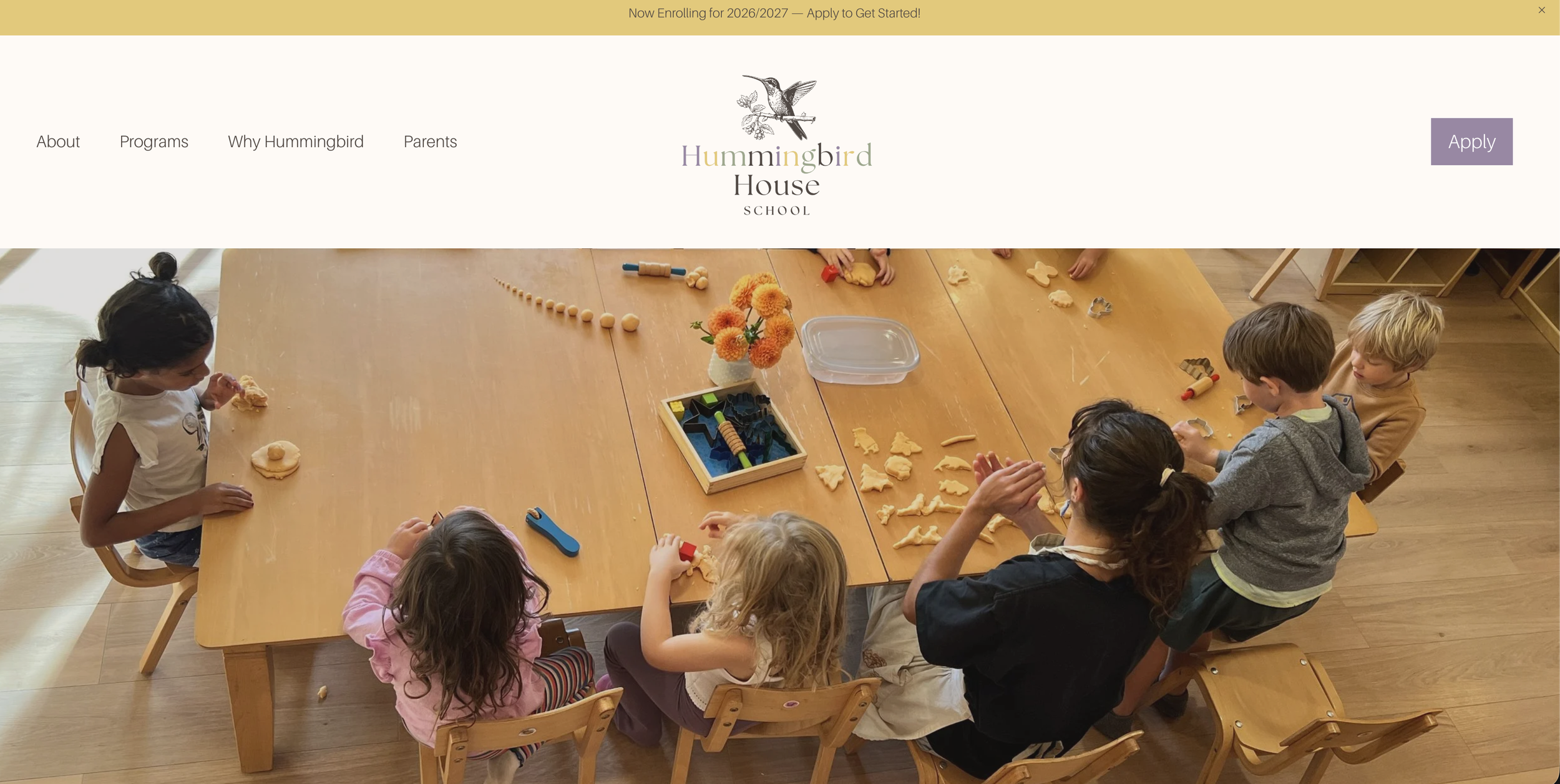 Children seated around a wooden table participating in a crafting activity, with various craft items and tools on the table.
