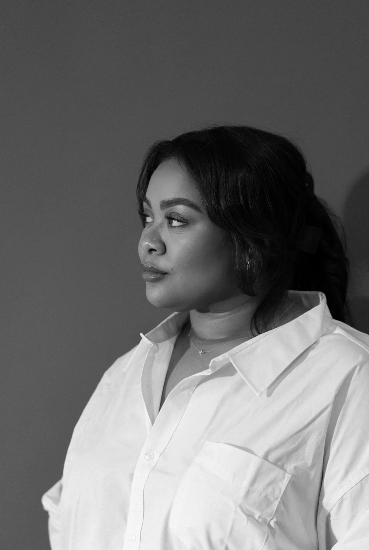 Black and white portrait of a woman with dark hair styled in waves, wearing a white button-up shirt, looking to her left.