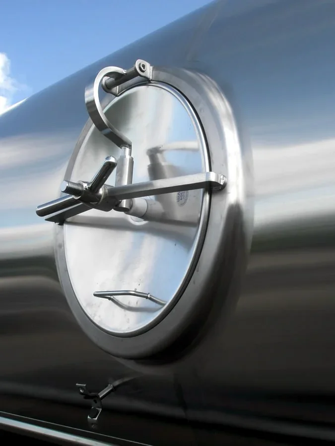 Close-up of a circular metal hatch with a handle and mechanical latch on a shiny metallic surface.