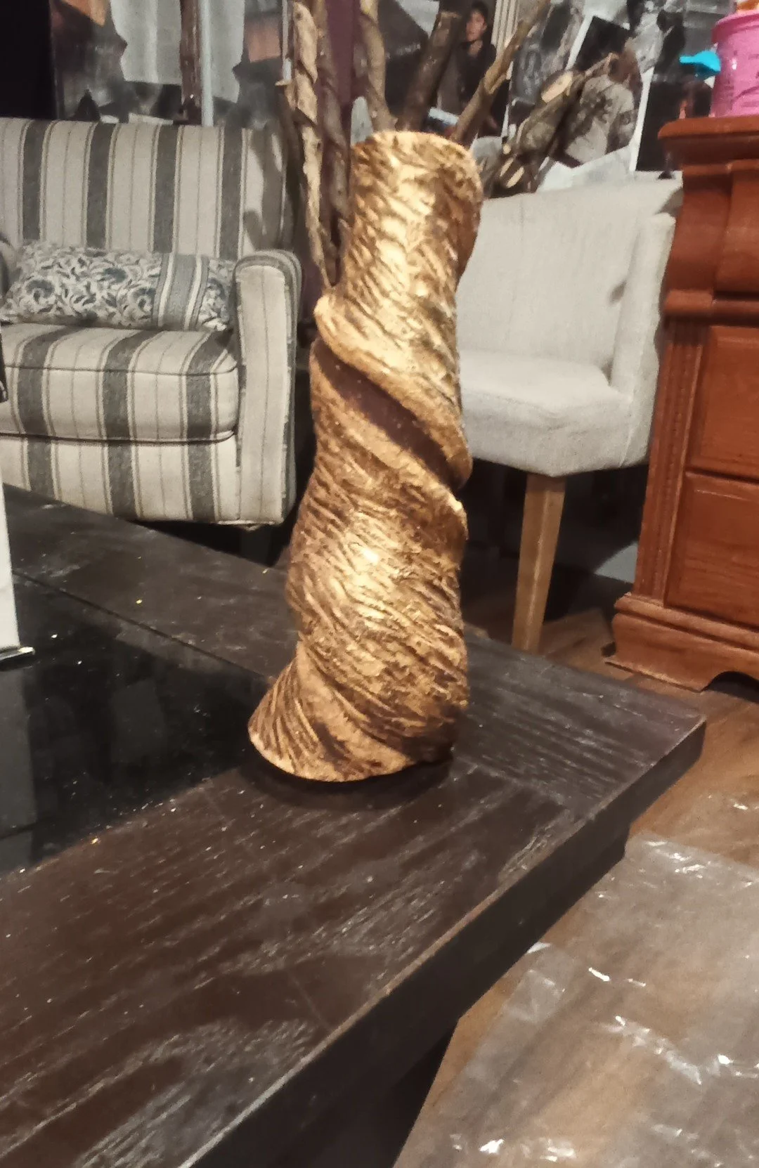 A wooden spiral sculpture on a dark wooden table in a room with couches and pictures on the wall.