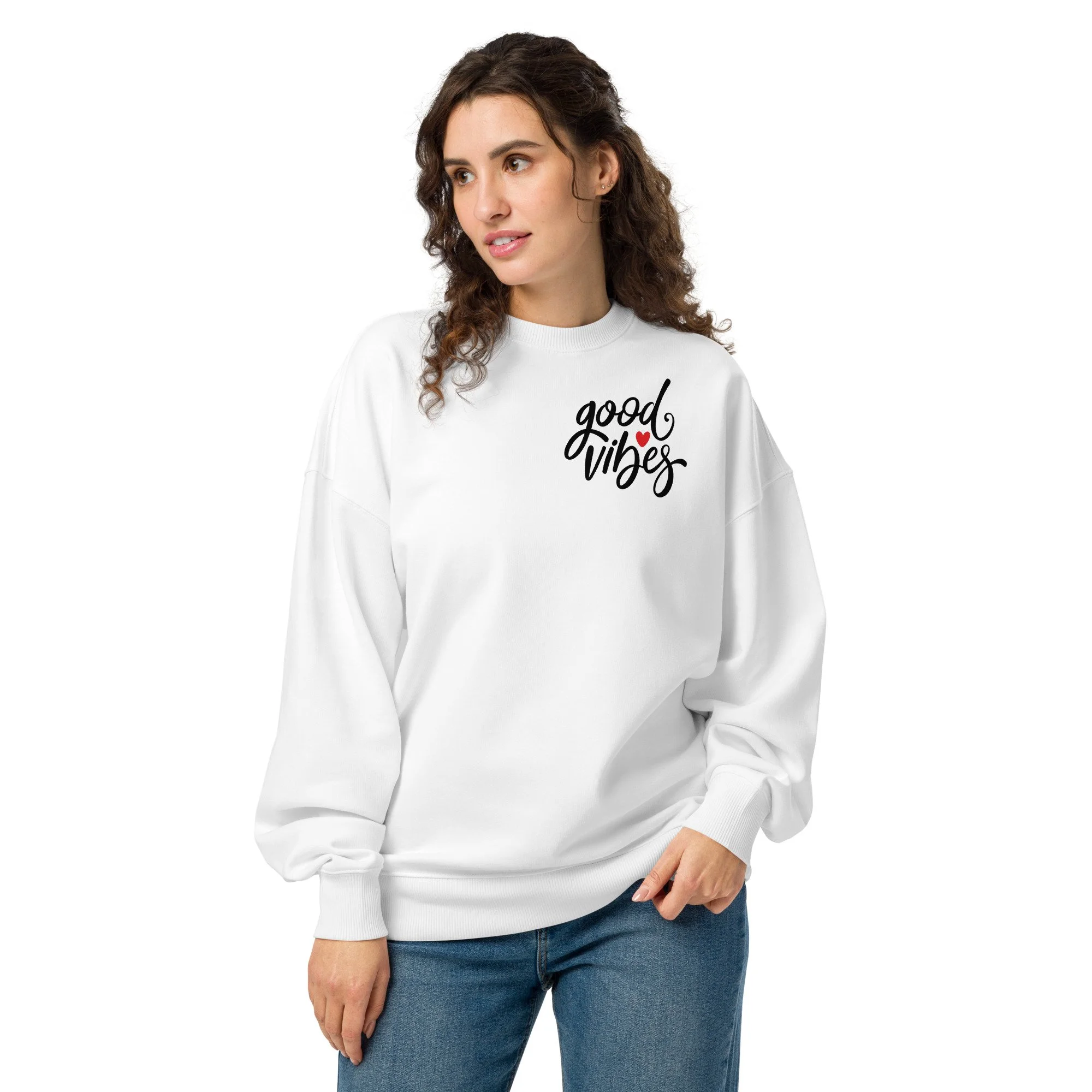 A woman with curly brown hair wearing a white sweatshirt with the words 'good vibes' and a red heart on it, standing against a white background.